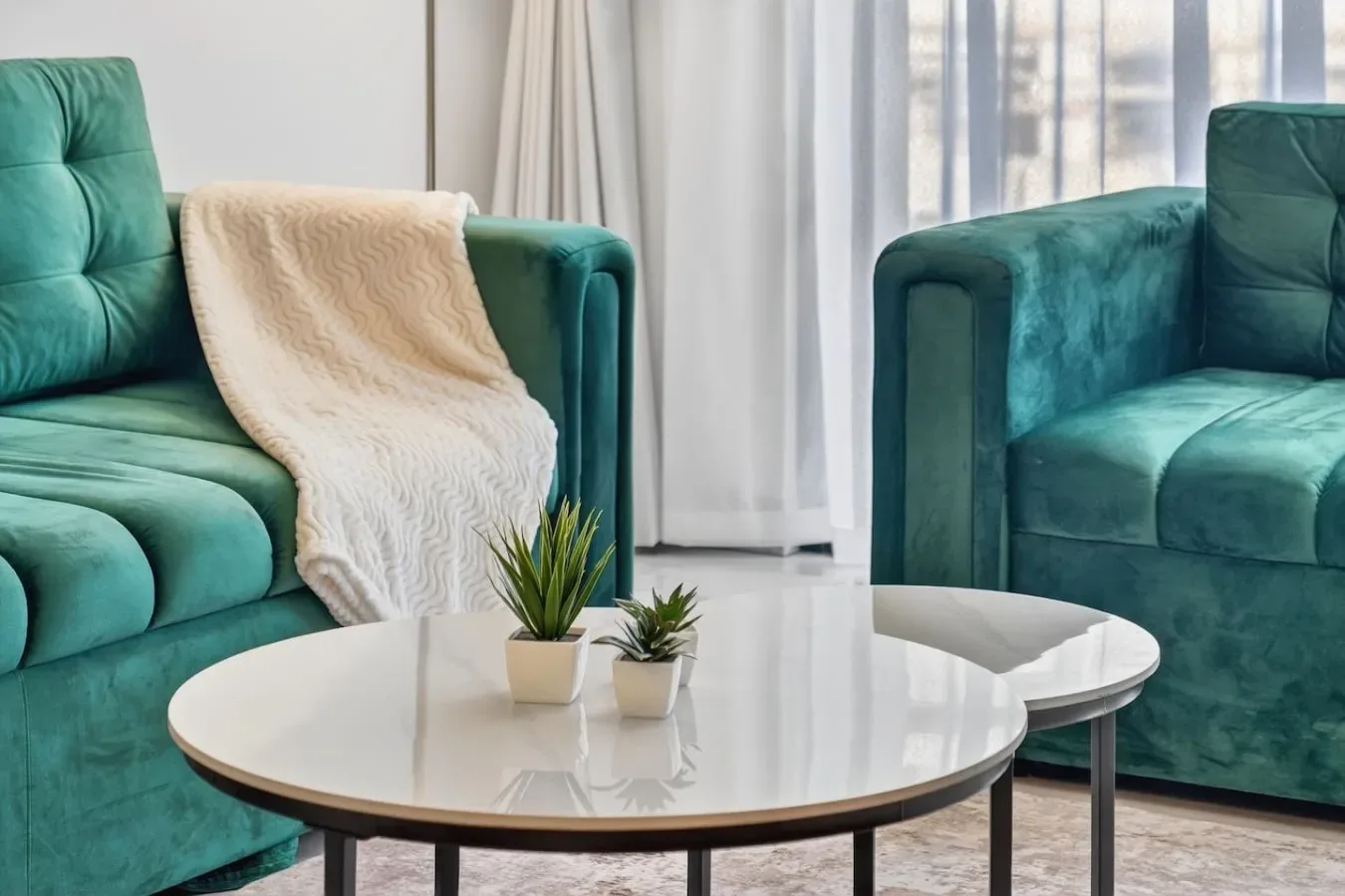 Una sala de estar con asientos color turquesa, una mesa de centro redonda y cortinas translúcidas.