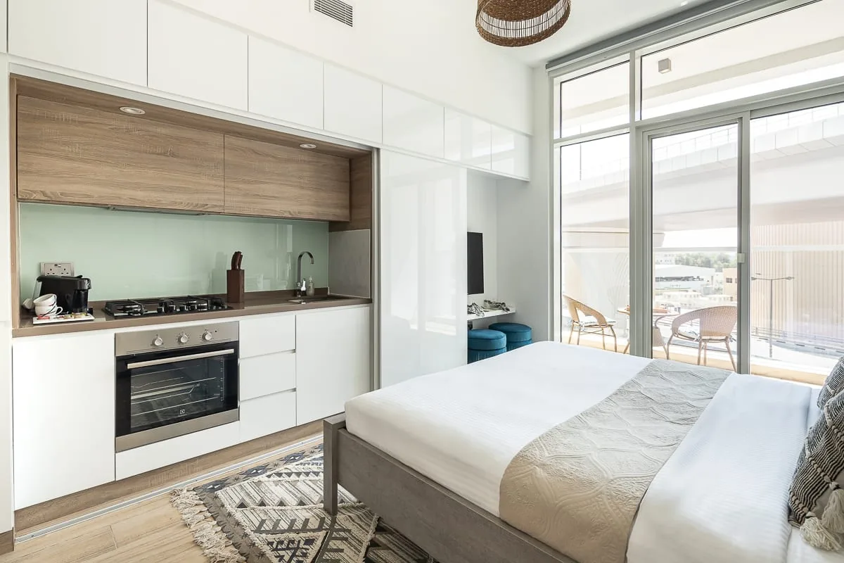 Un dormitorio luminoso con una cama junto a una cocina compacta y grandes puertas de vidrio.