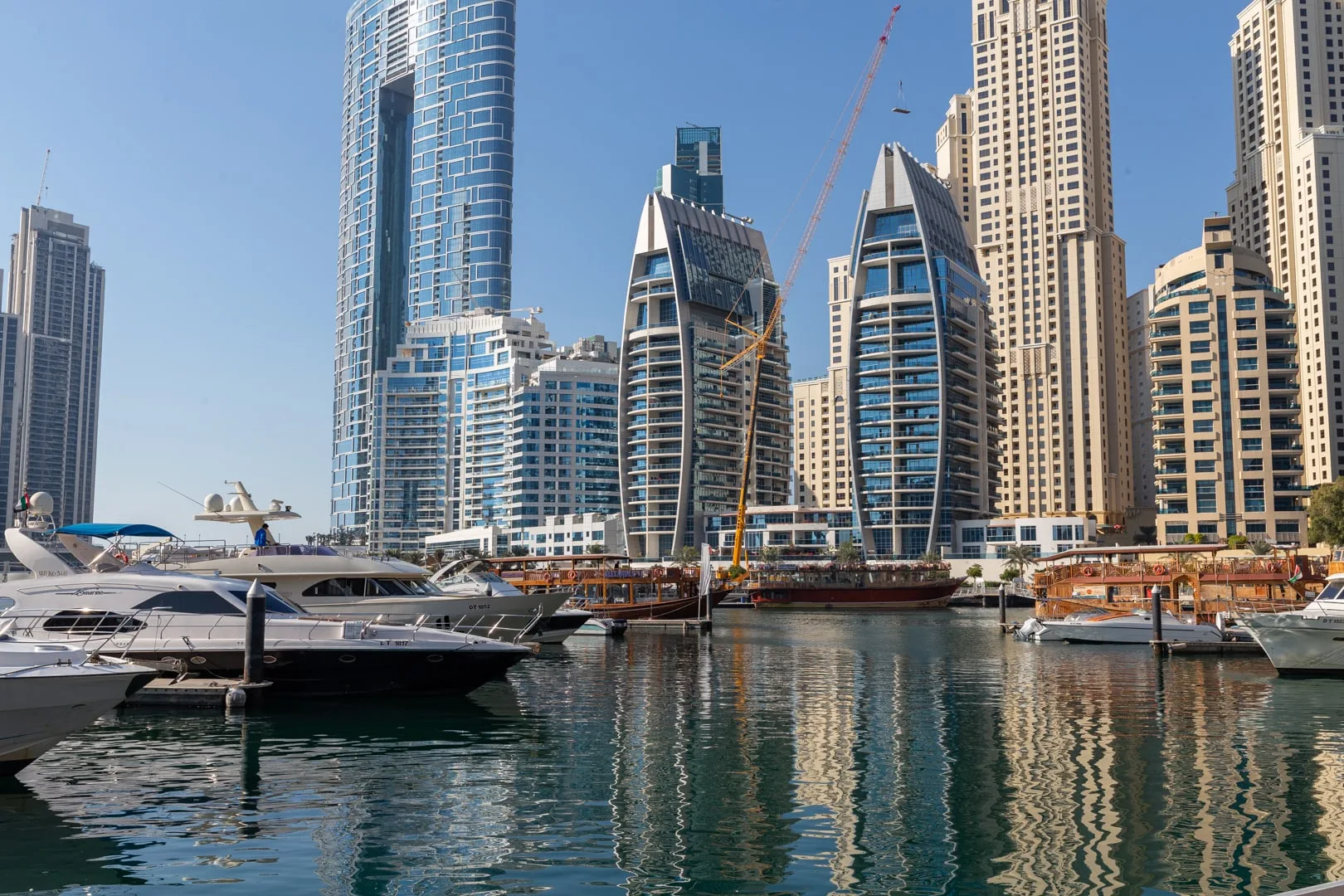 A marina with yachts sits in front of a waterfront skyline of tall buildings.