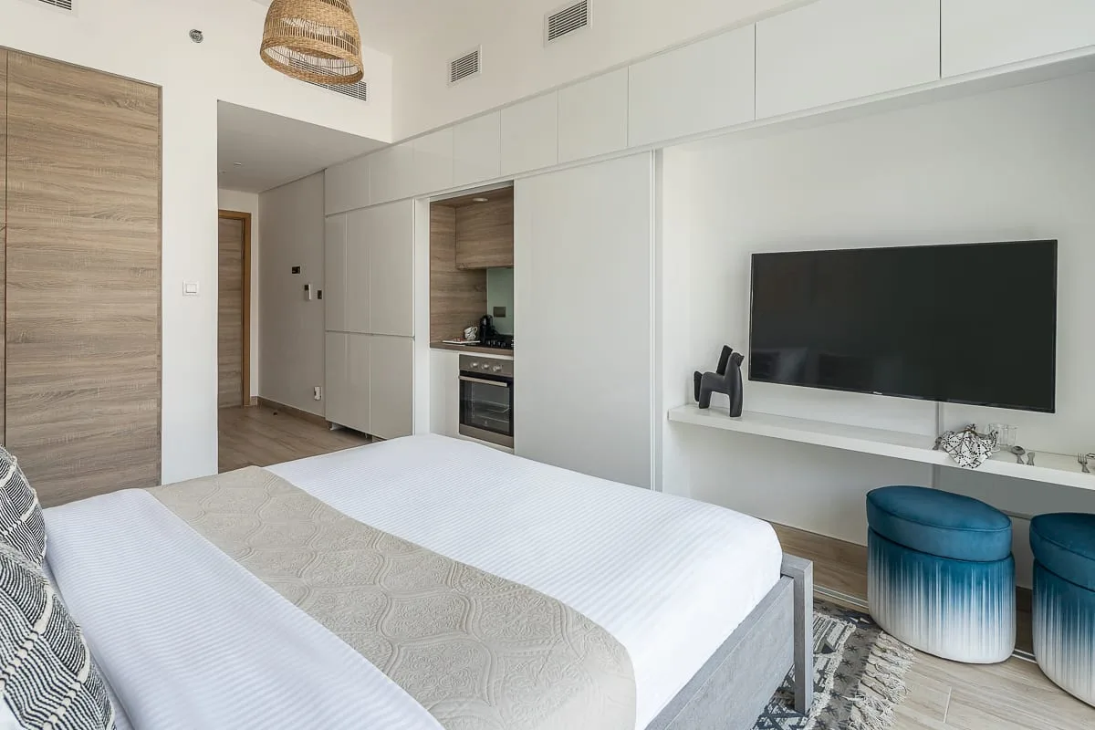A bright bedroom with a bed, built-in cabinetry, and a wall-mounted television.