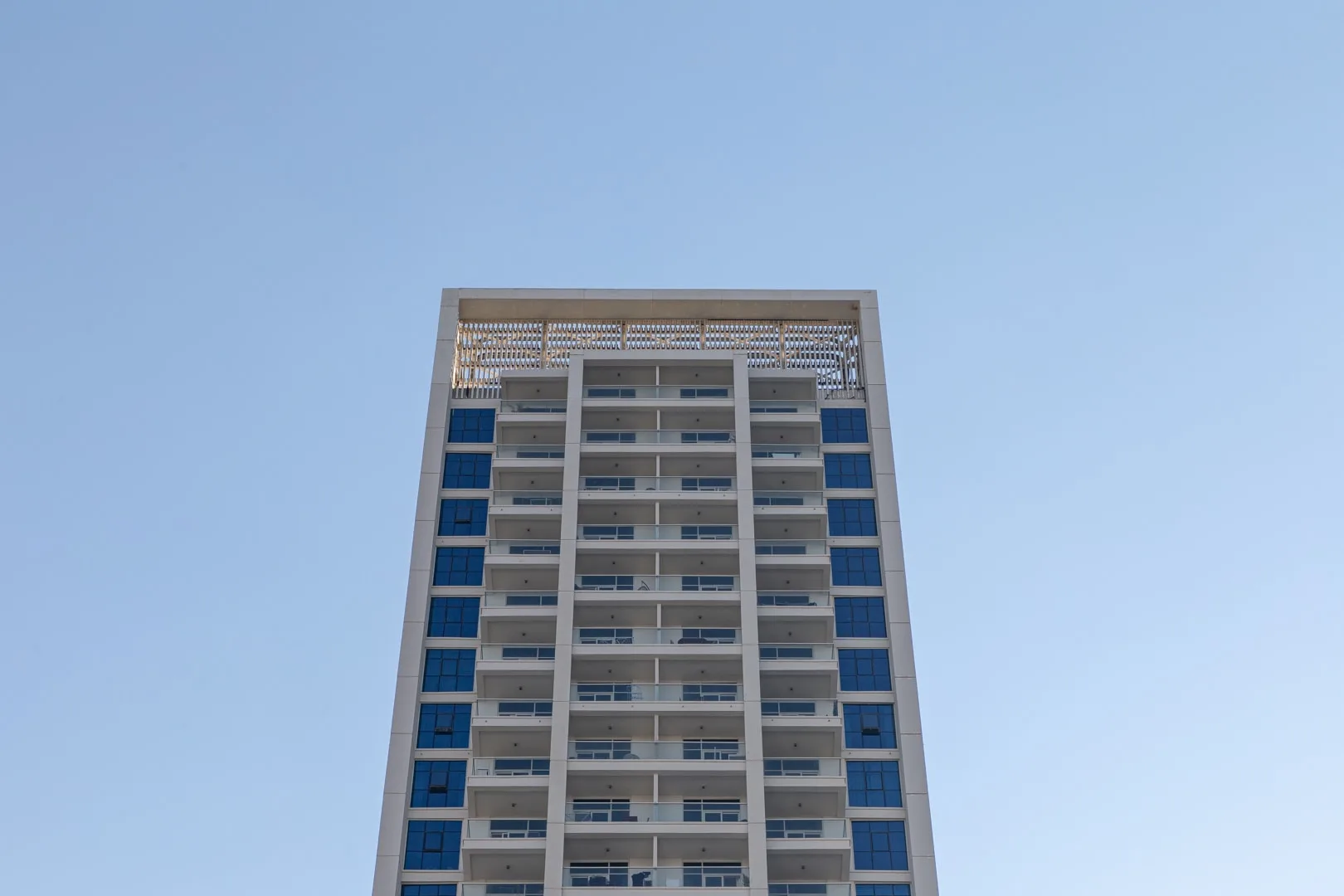 A tall modern building with rows of windows stands against a clear sky.