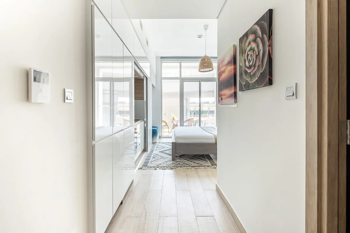 A bright bedroom is visible beyond a hallway, with a bed and wall art.