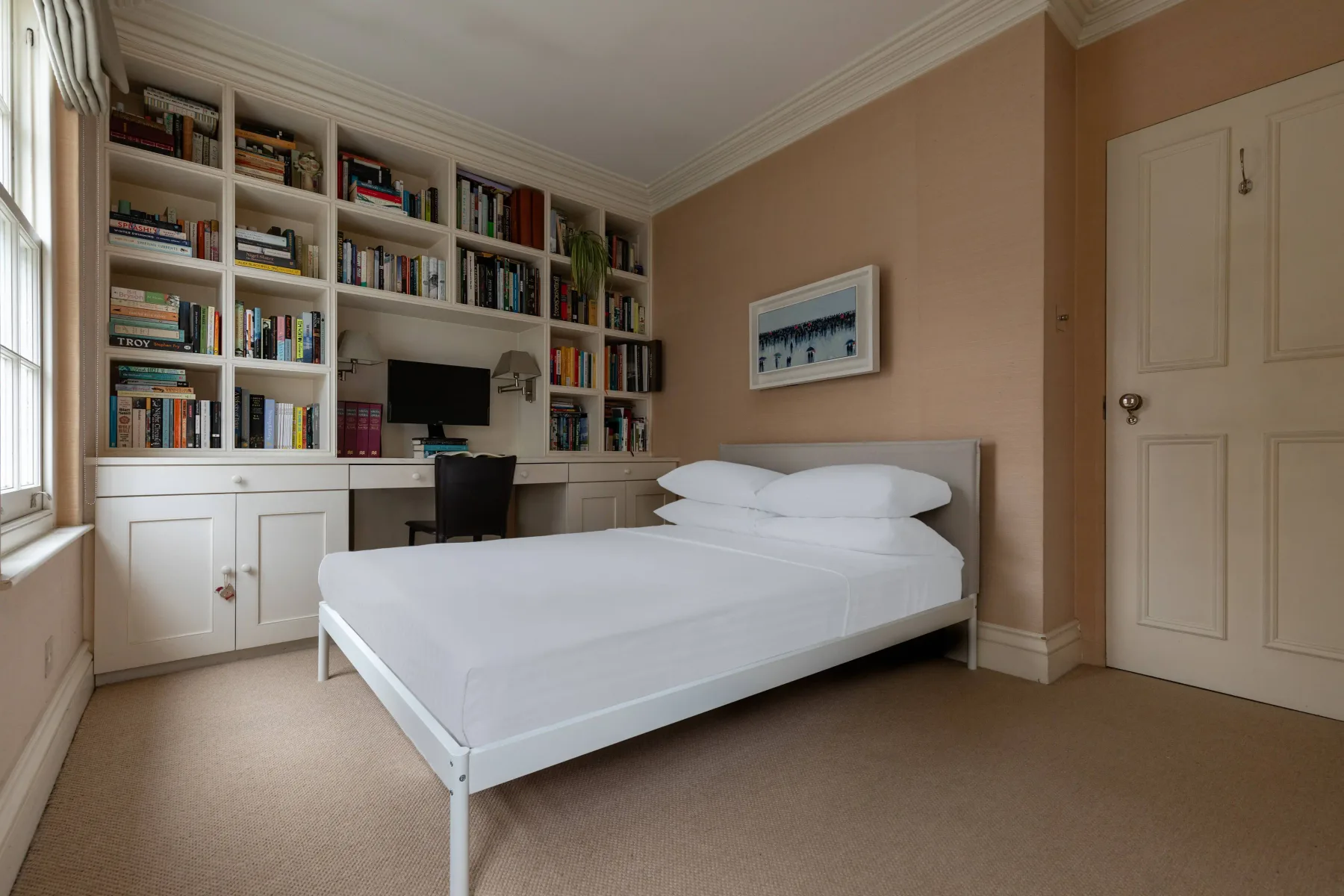 A bedroom with a bed beside built-in bookshelves and a desk.
