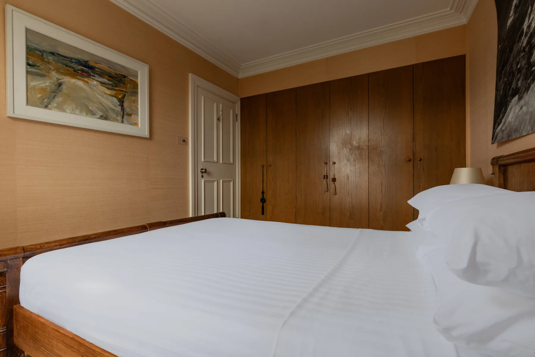 A bedroom with a neatly made bed and a row of wooden wardrobes.