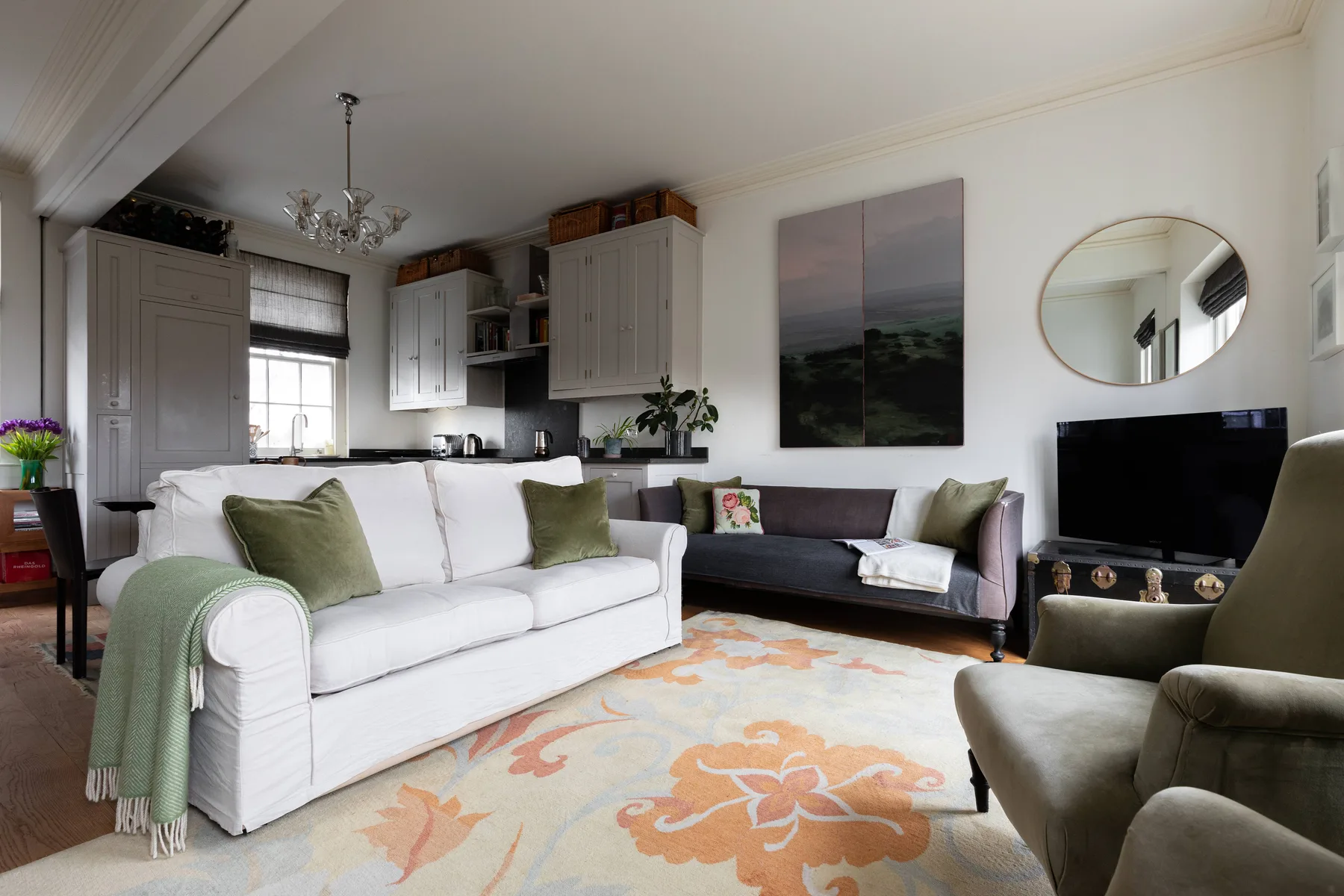 A living room with white seating, a patterned rug, and a television.