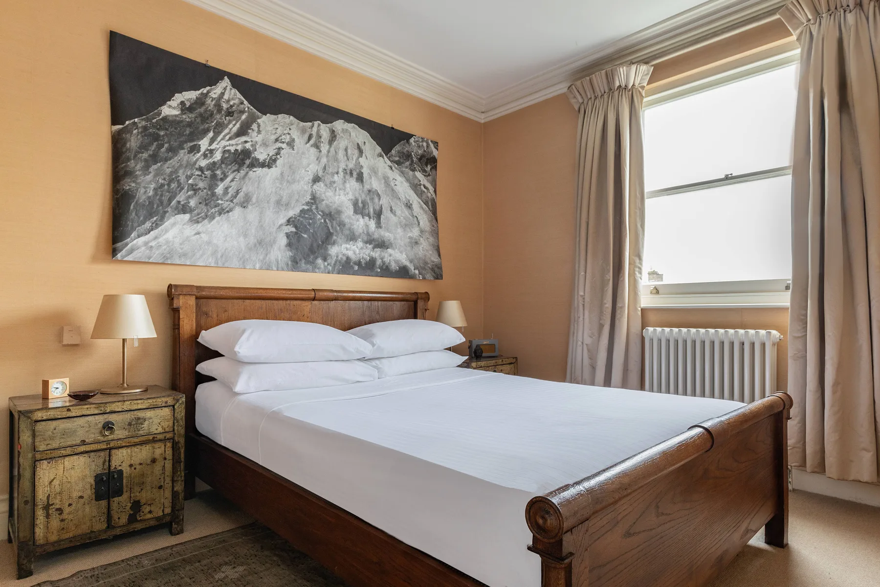A bedroom with a wooden bed beneath a large black-and-white mountain photograph.