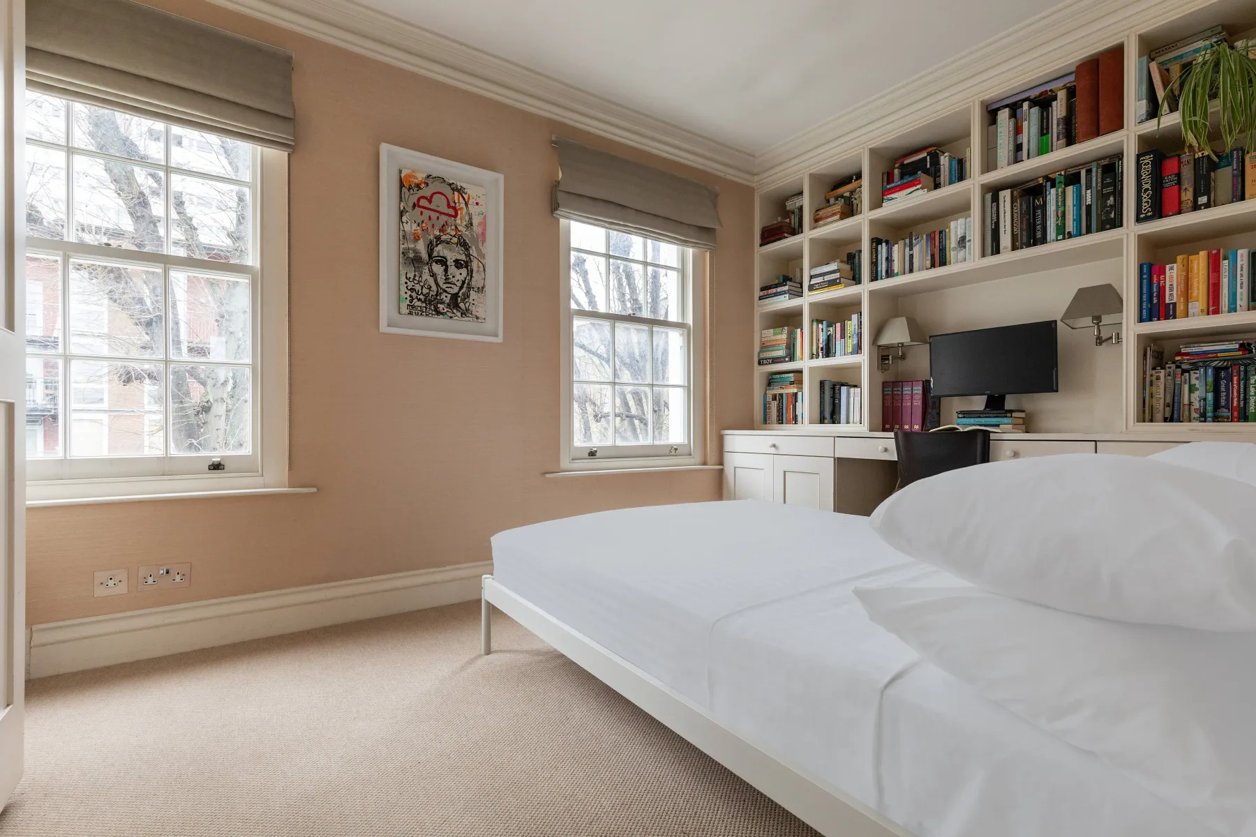 A bedroom with a bed, windows, and built-in bookshelves.