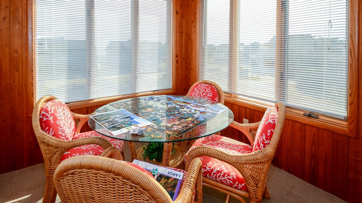 Comedor en un solárium con mesa de vidrio y asientos de mimbre.