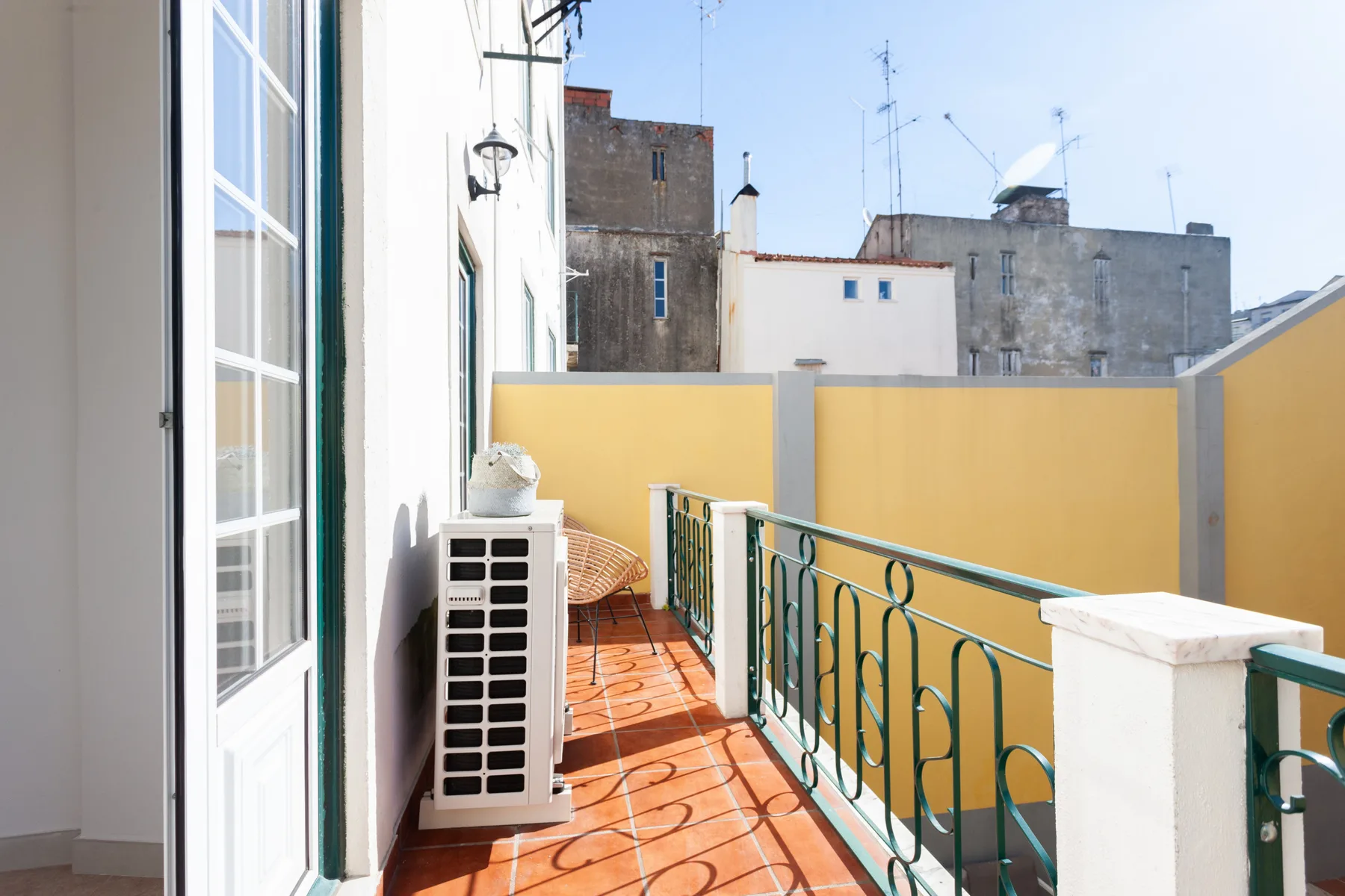 A narrow balcony with terracotta tiles and green metal railings.