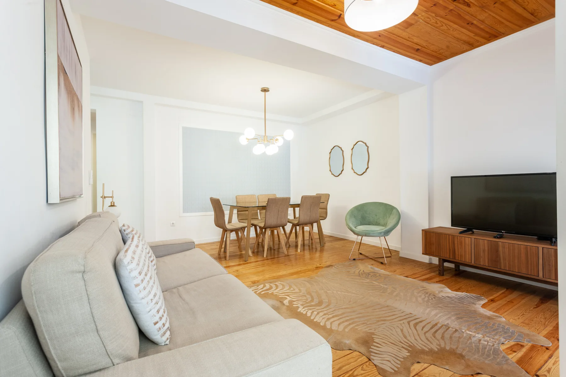 A bright living and dining room with seating, a television, and a wooden ceiling.