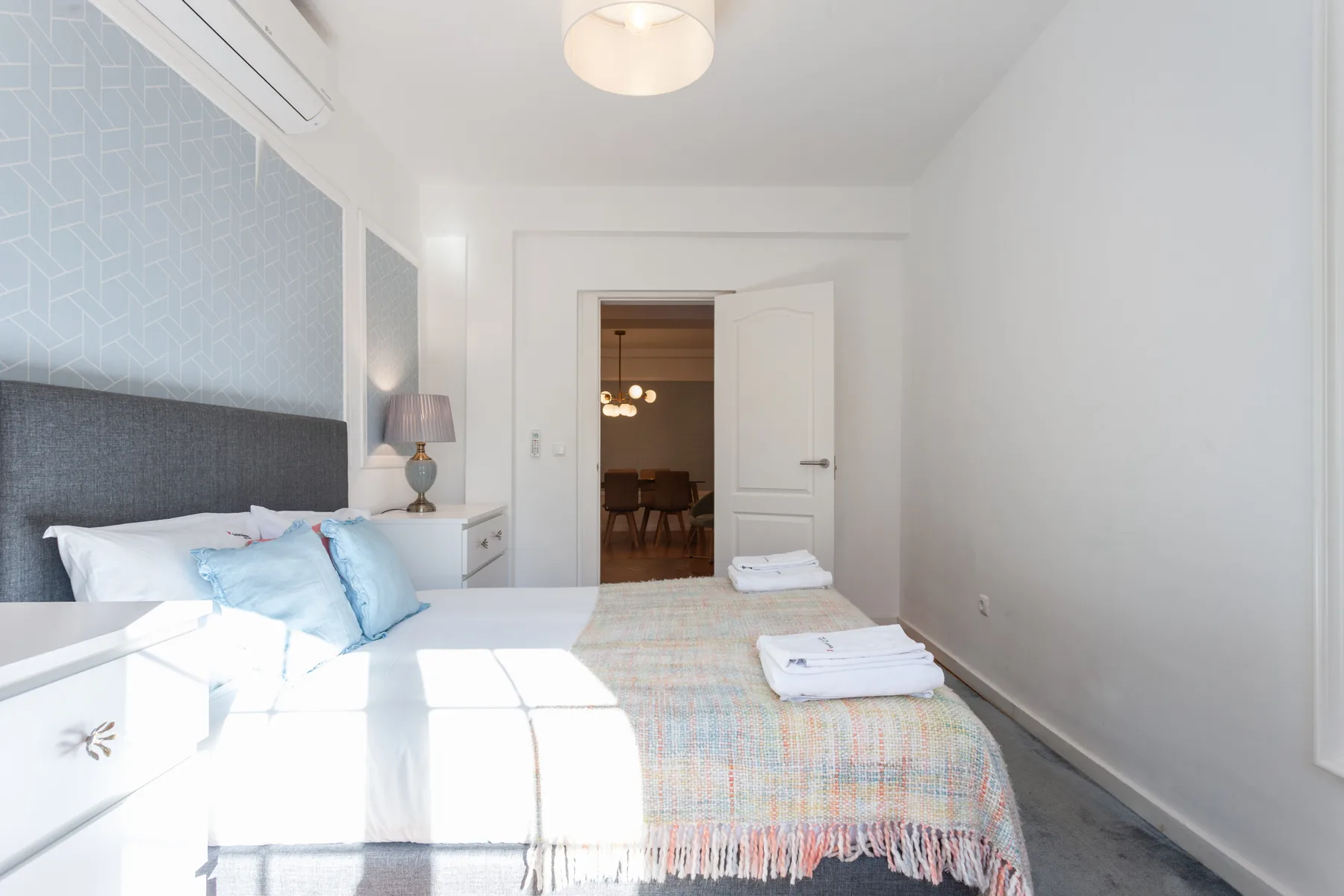A bright bedroom with a bed and an open doorway leading to a dining area.