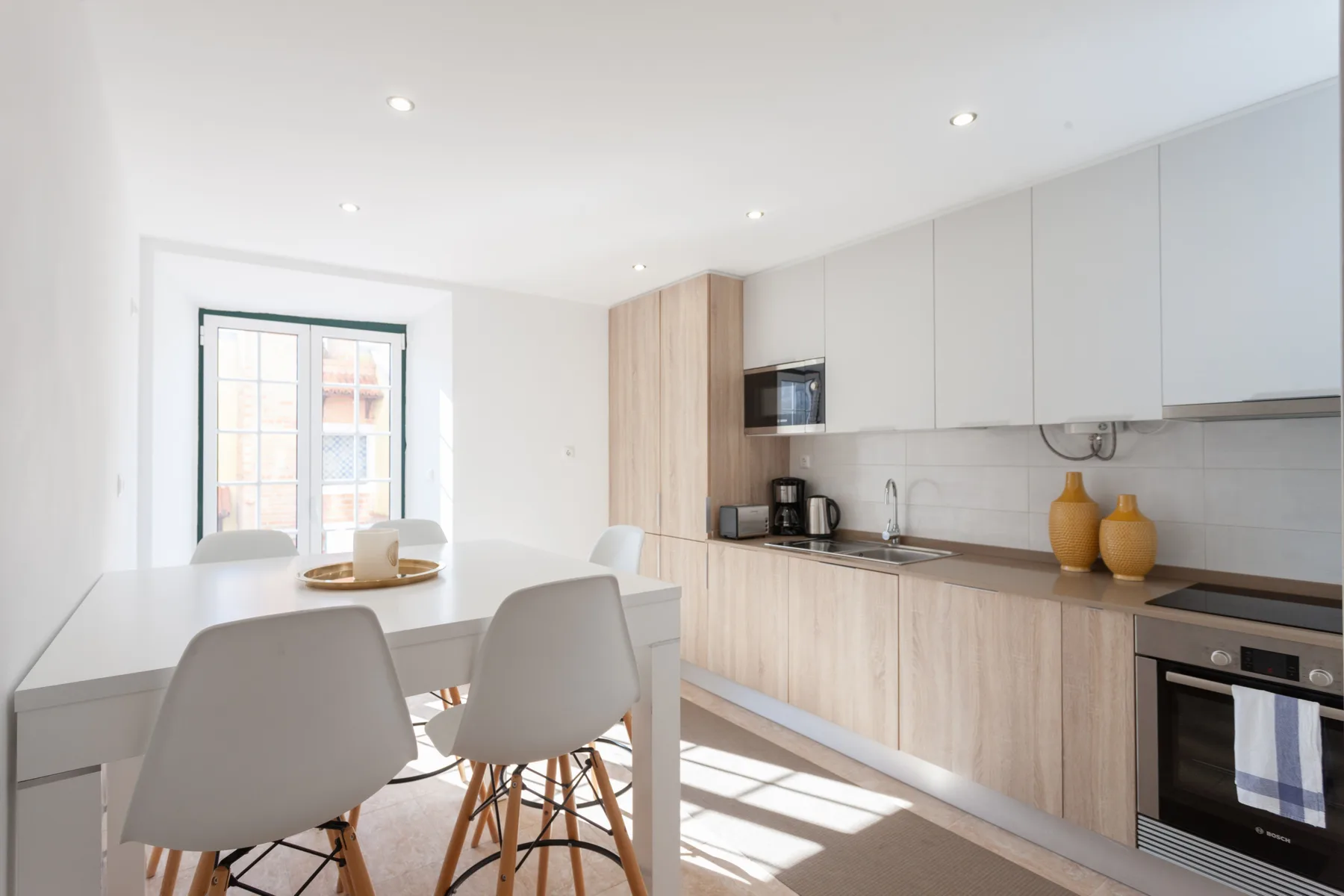A bright dining area and kitchen with a table beside a large window.