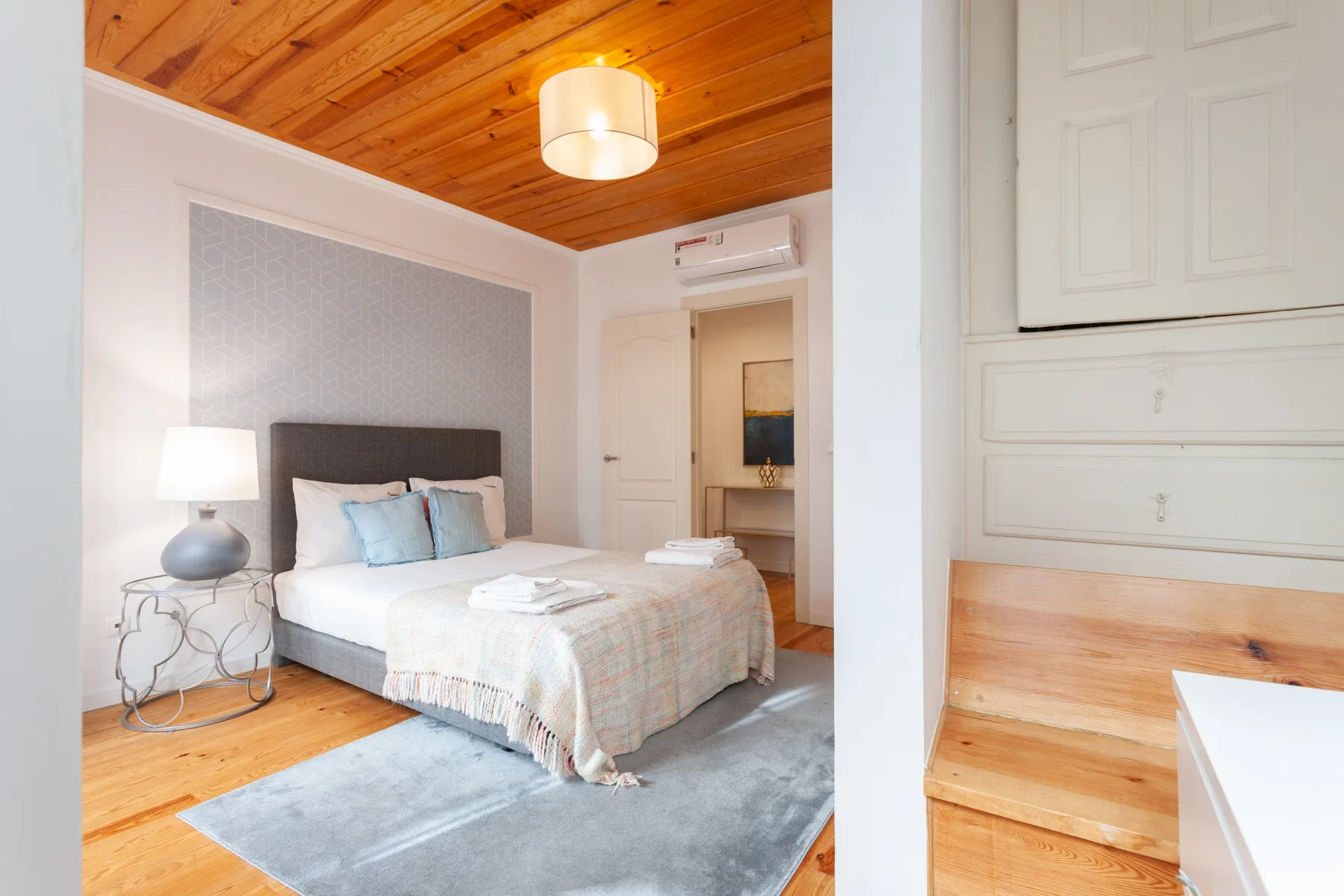 A bedroom with a neatly made bed and a wooden ceiling.