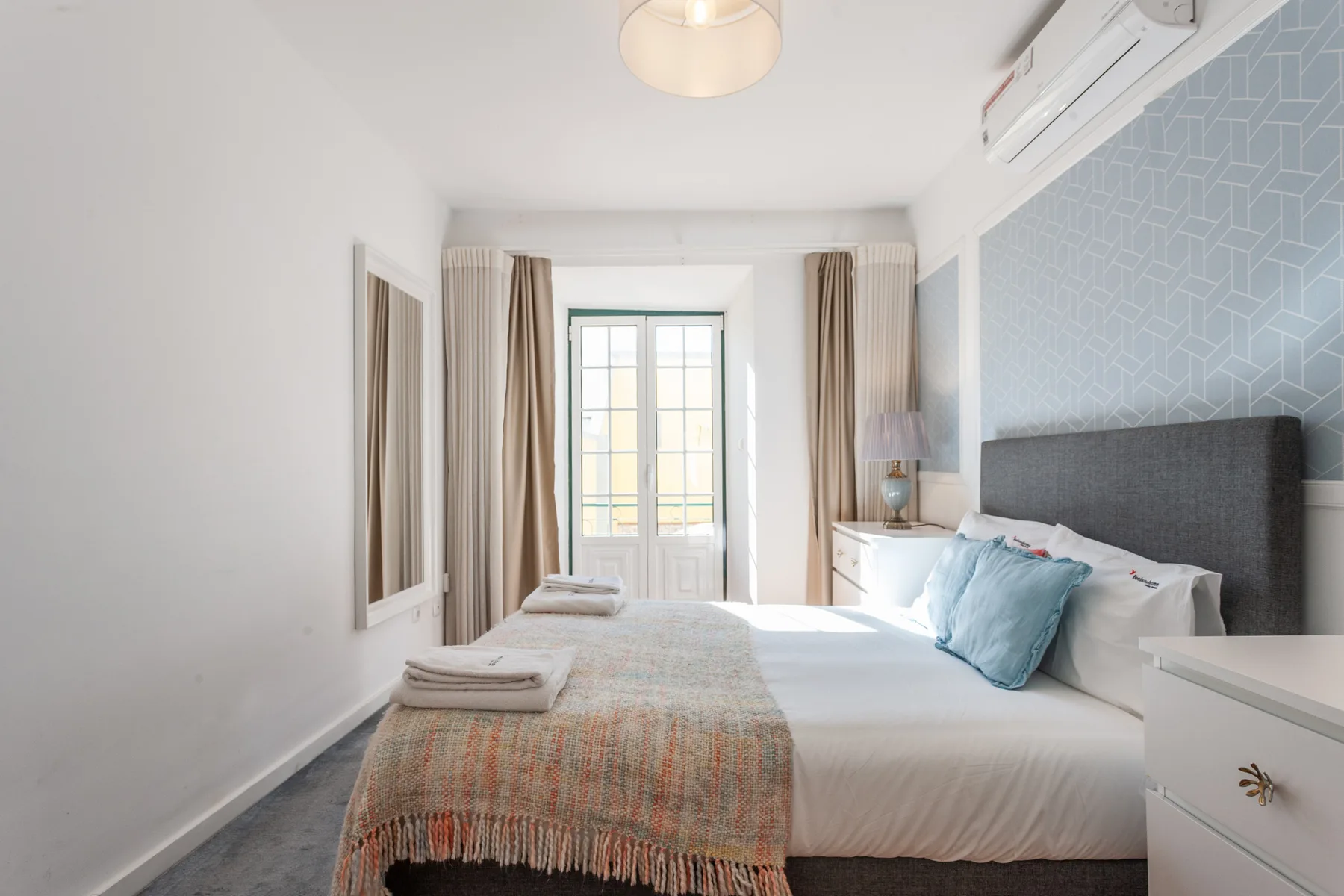 A bright bedroom with a bed and tall windows framed by curtains.