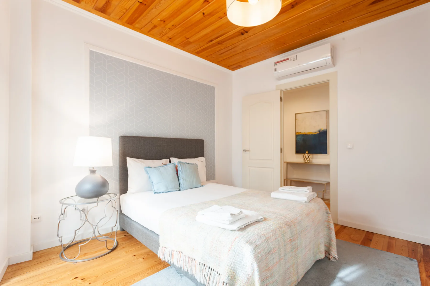 A bedroom with a double bed, bedside table, and wooden ceiling.