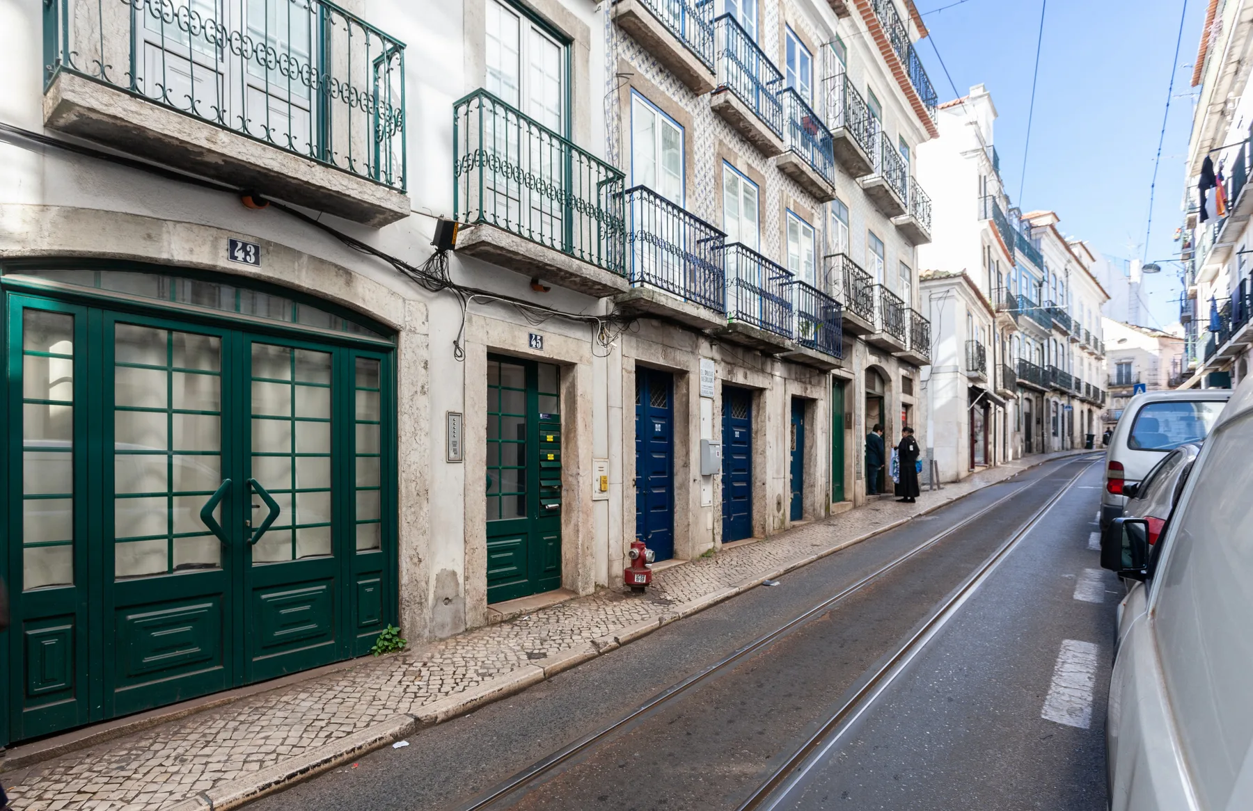 A narrow city street lined with apartment buildings and parked cars.