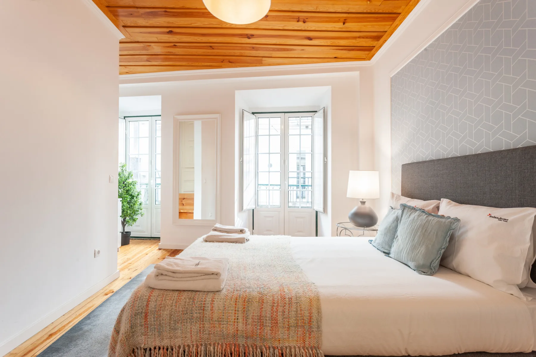 A bright bedroom with a large bed, patterned accent wall, and wood ceiling.