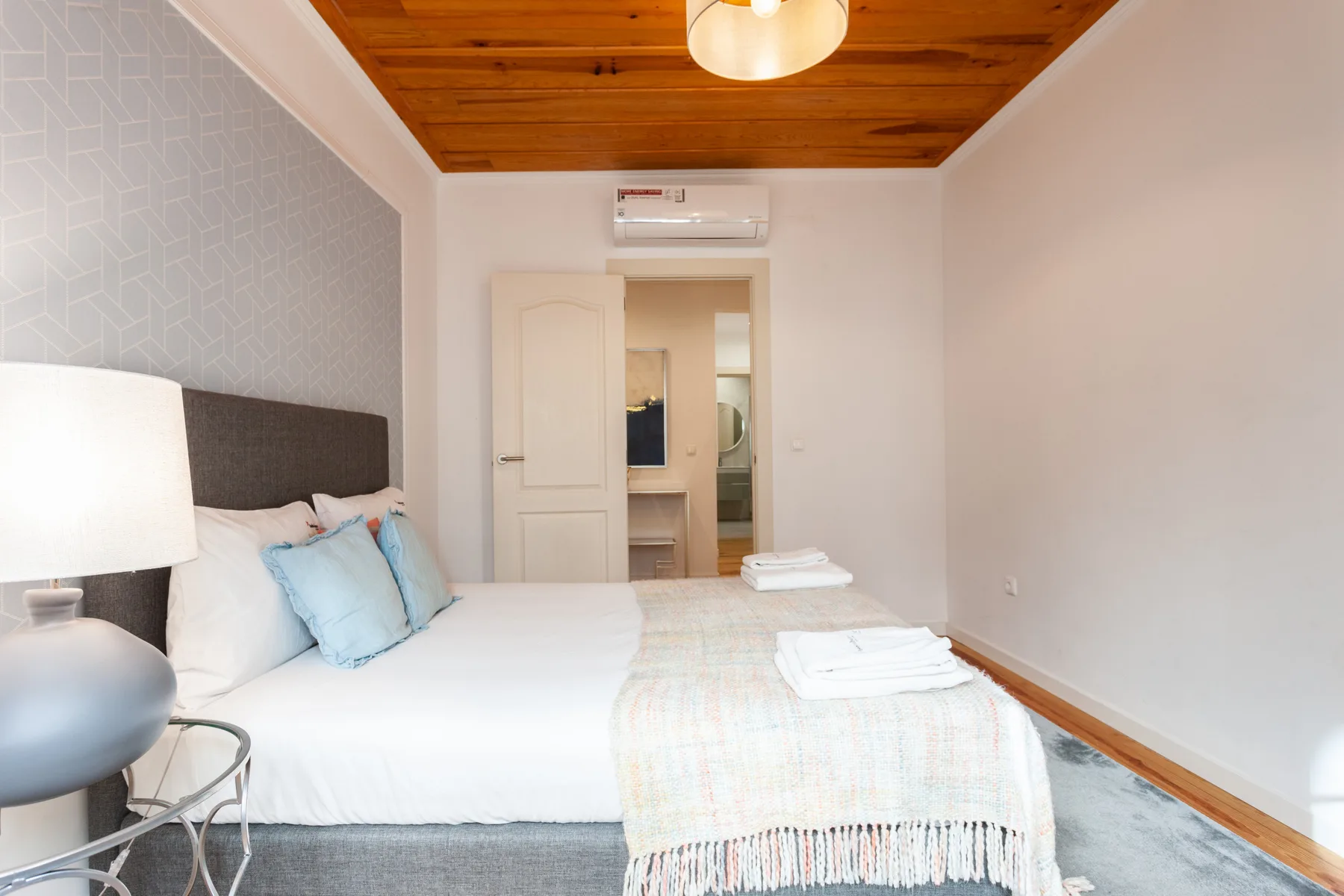 A bedroom with a neatly made bed, folded towels, and a doorway to another room.
