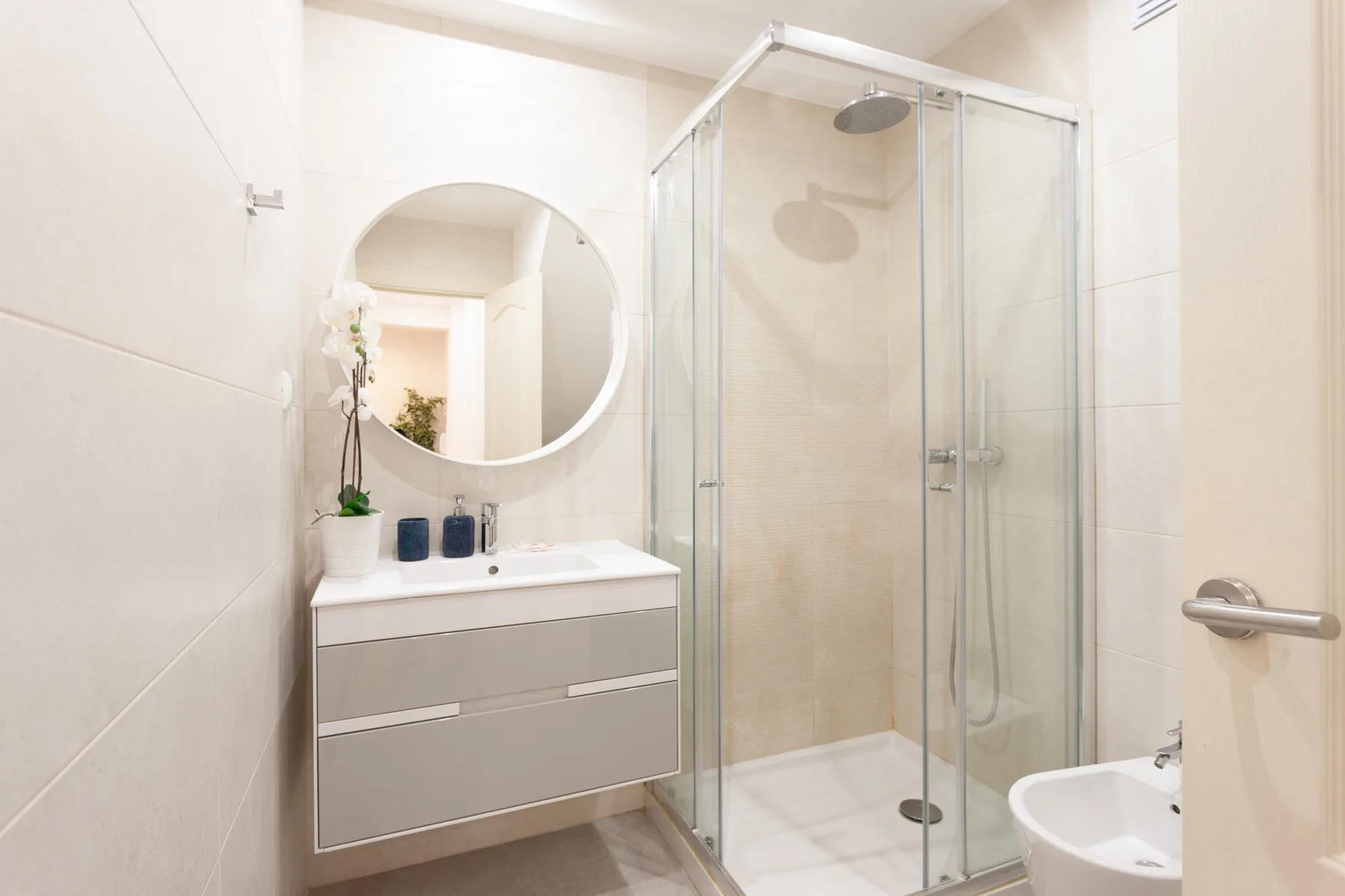 A bright bathroom with a vanity, round mirror, and shower.