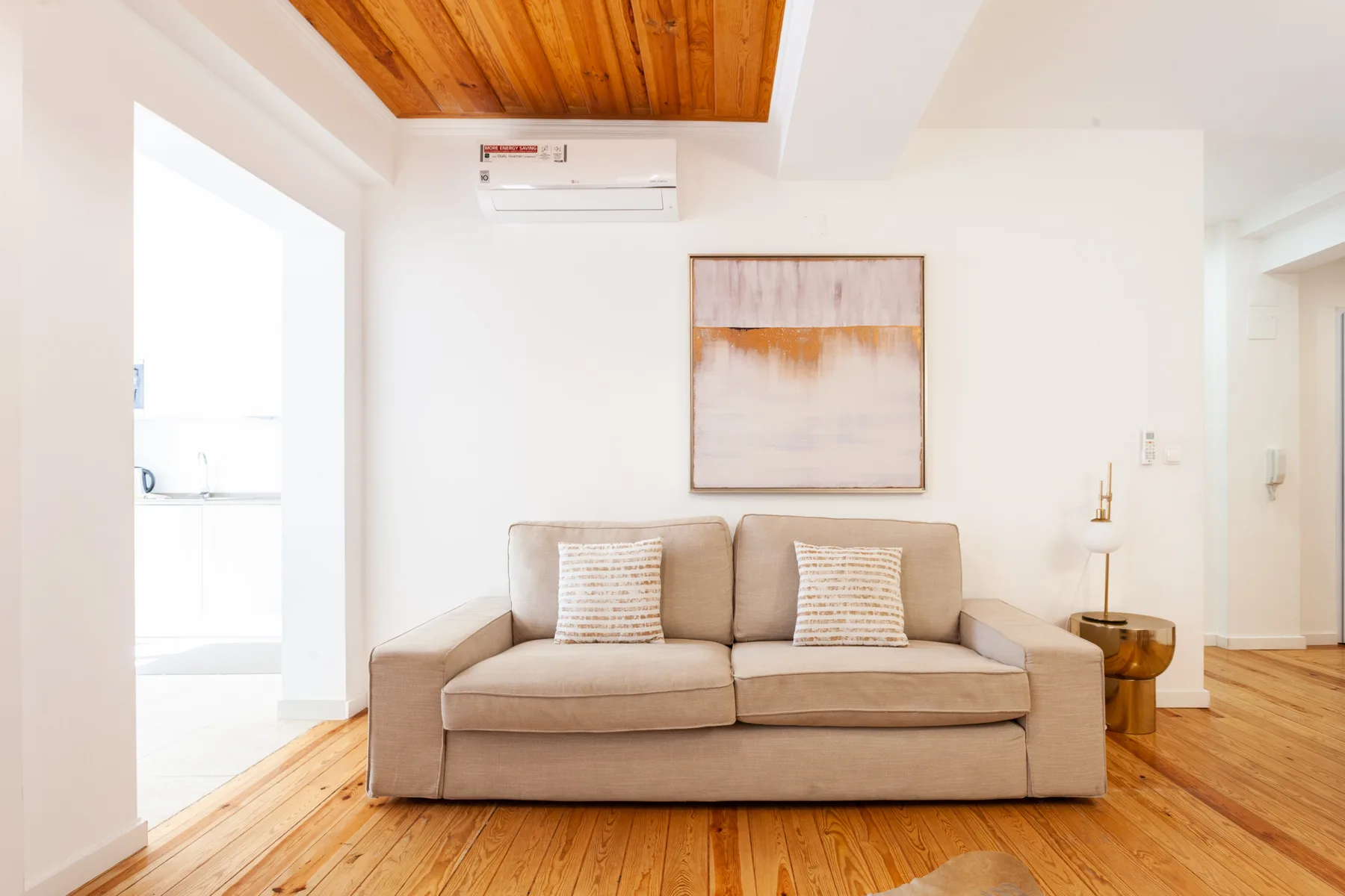 A living room with a beige sofa beneath a wall-mounted air conditioner.