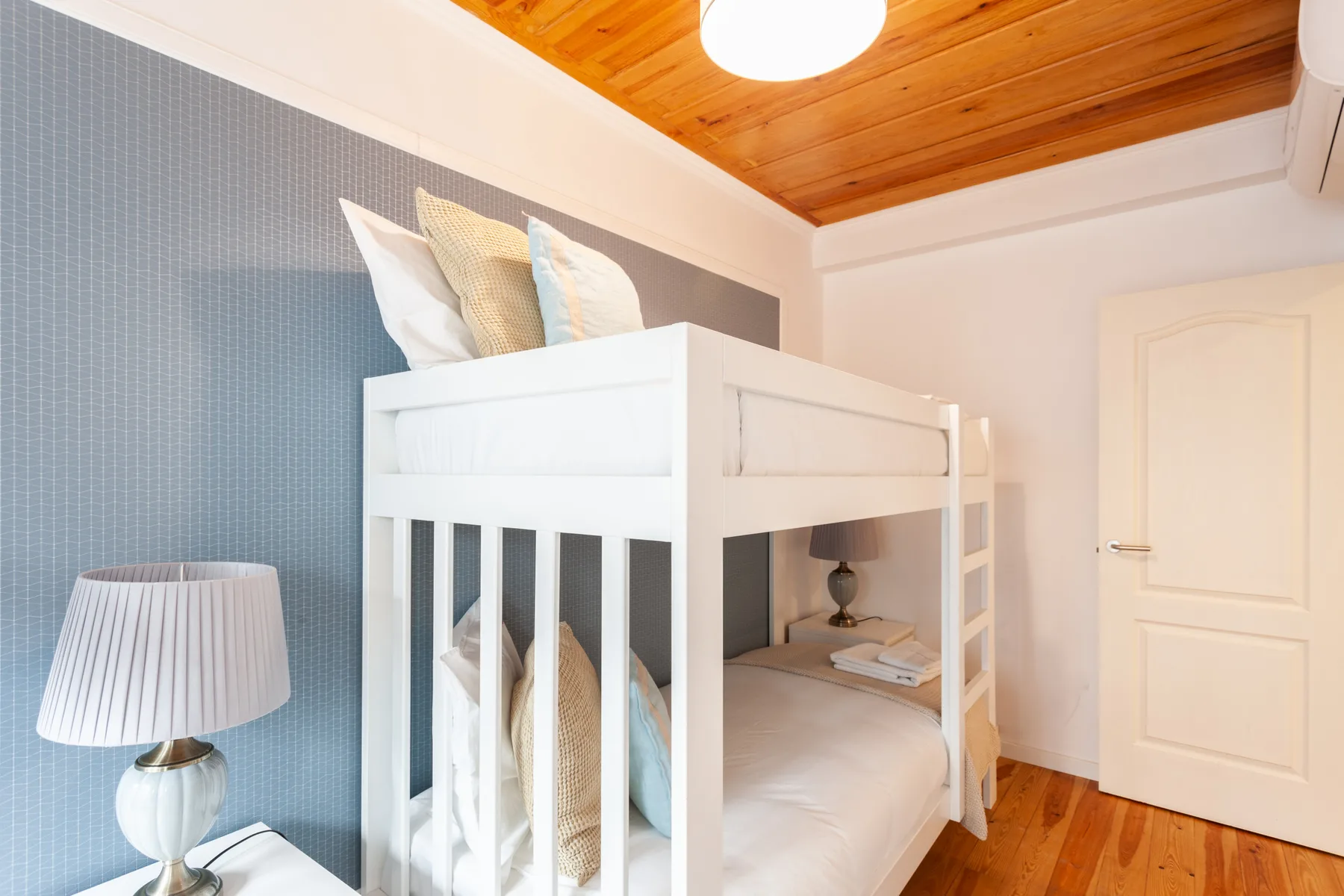A bedroom with white bunk beds and a wooden ceiling.