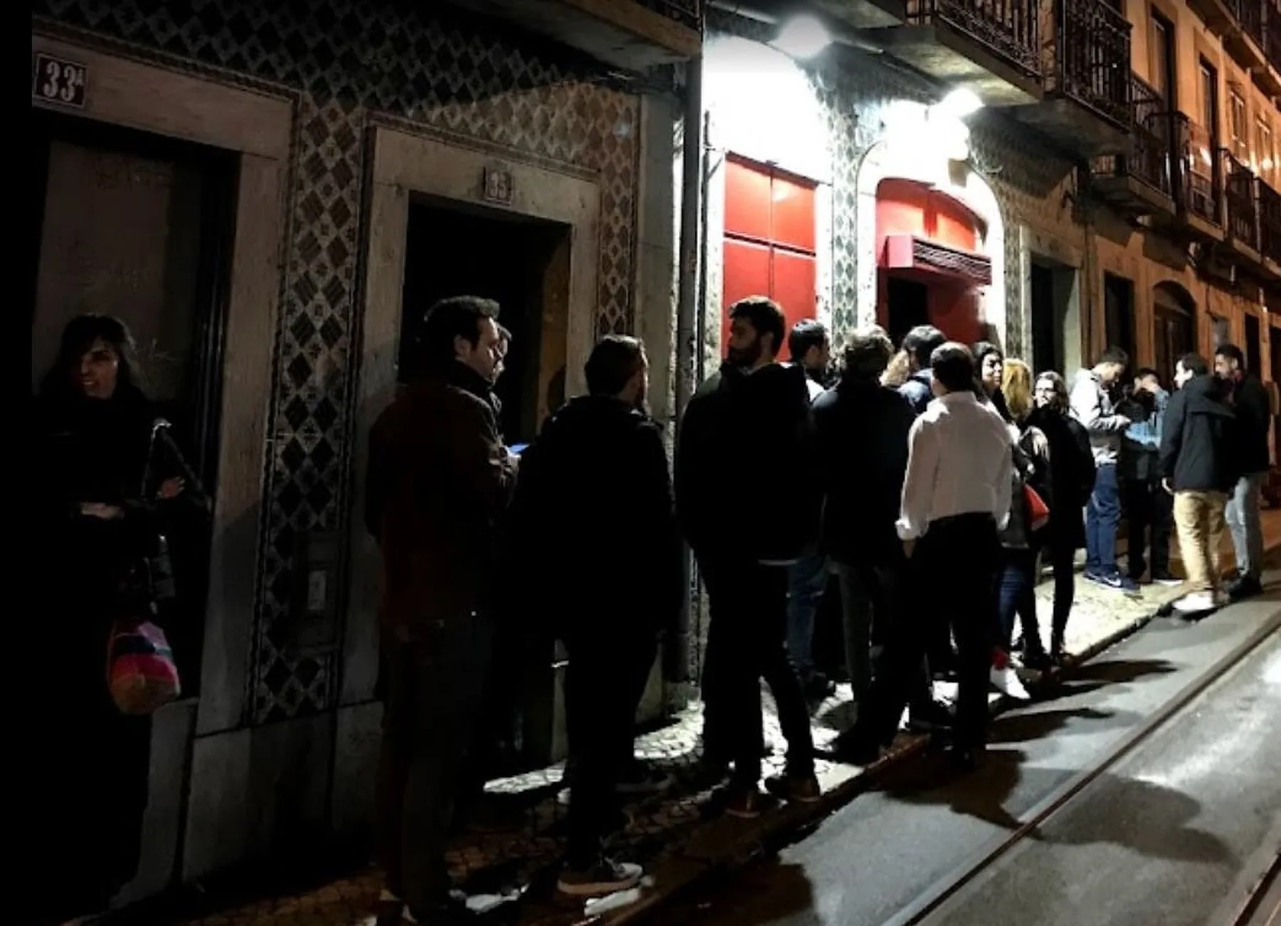 A nighttime street scene shows people gathered outside a brightly lit storefront.