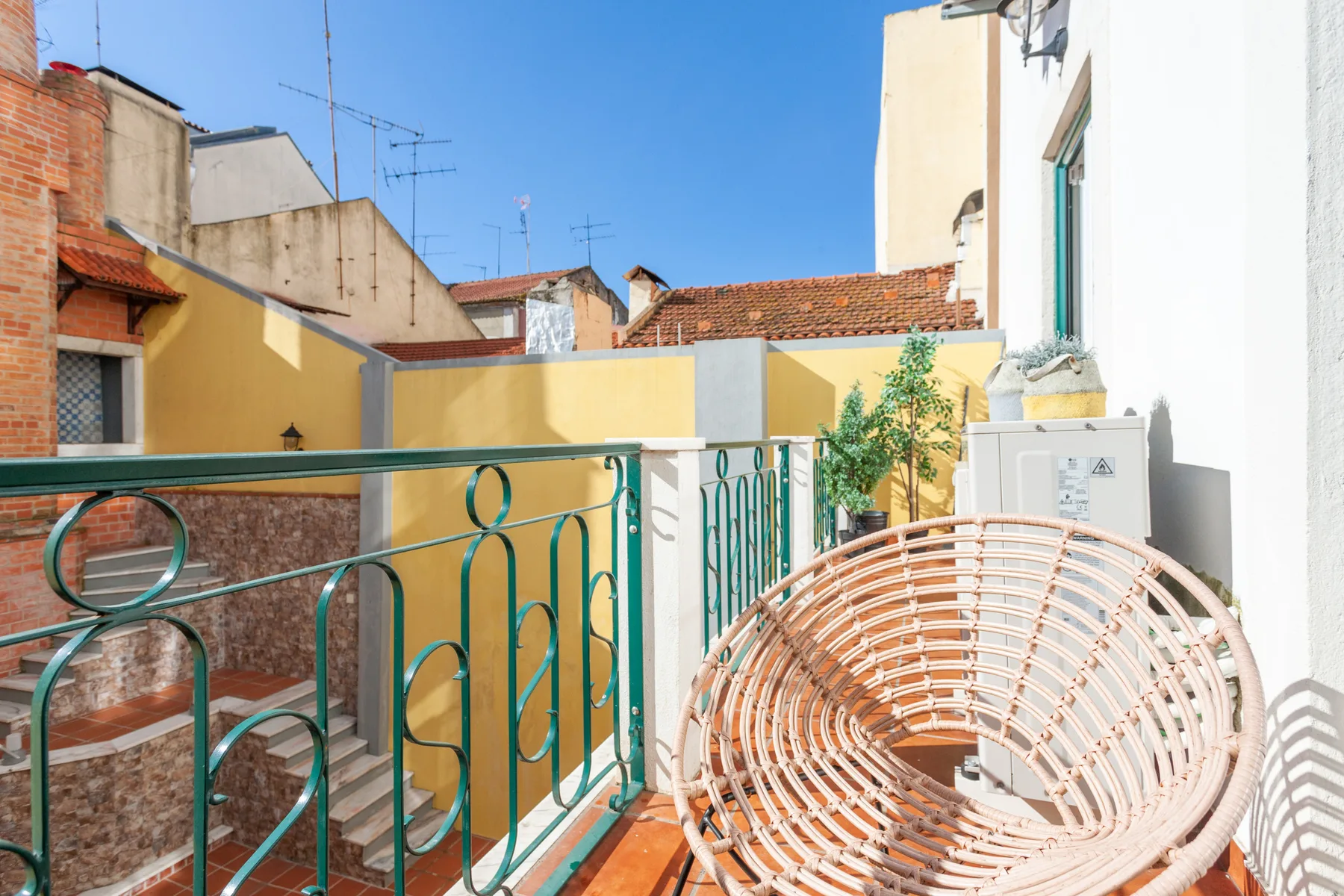 A small balcony with a woven seating chair and green metal railing.