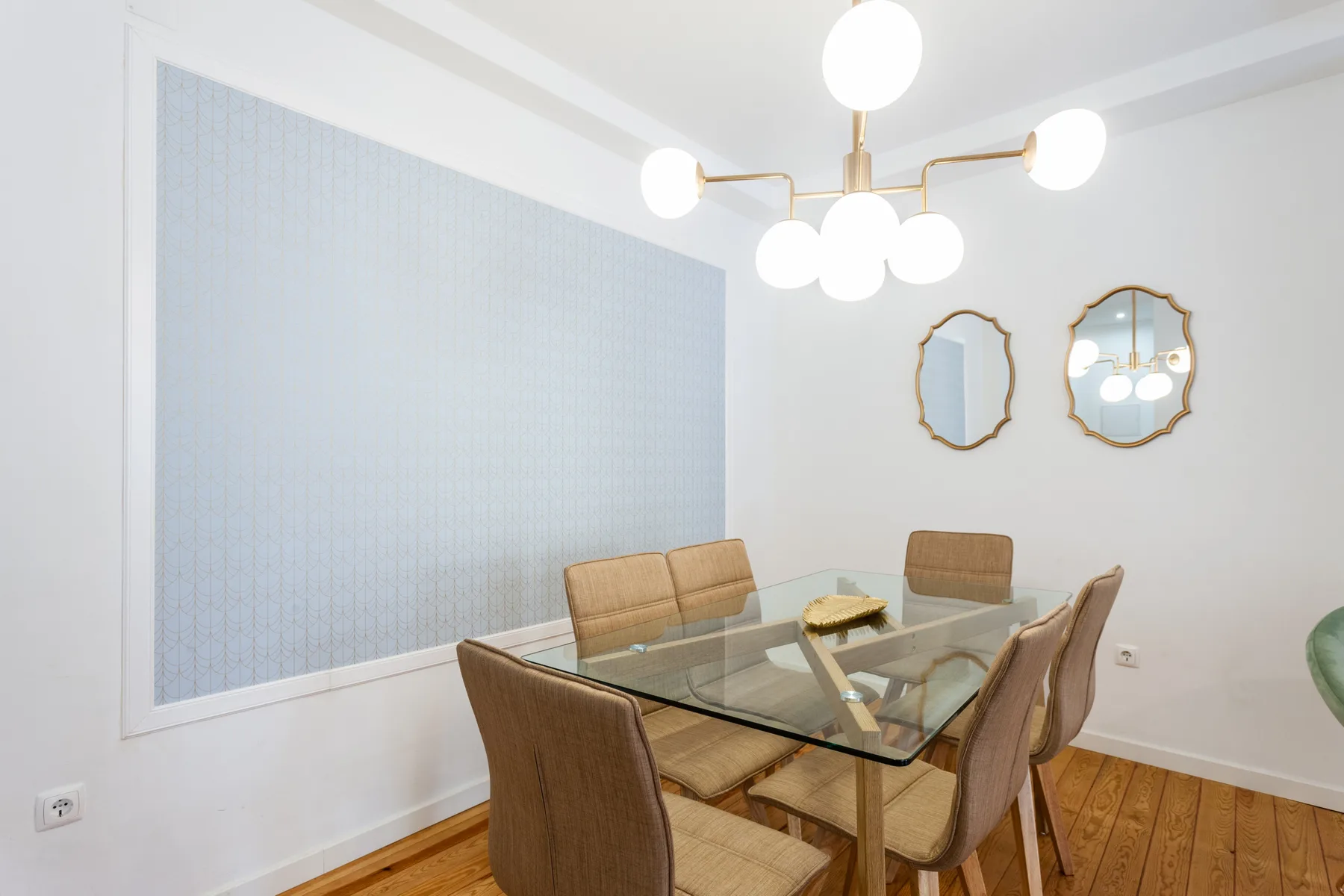 Dining area with a glass table, upholstered seating, and two wall mirrors.