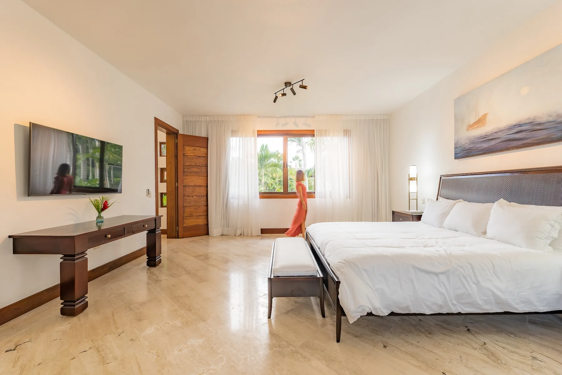 A bright bedroom with a large bed, a window, and a television.
