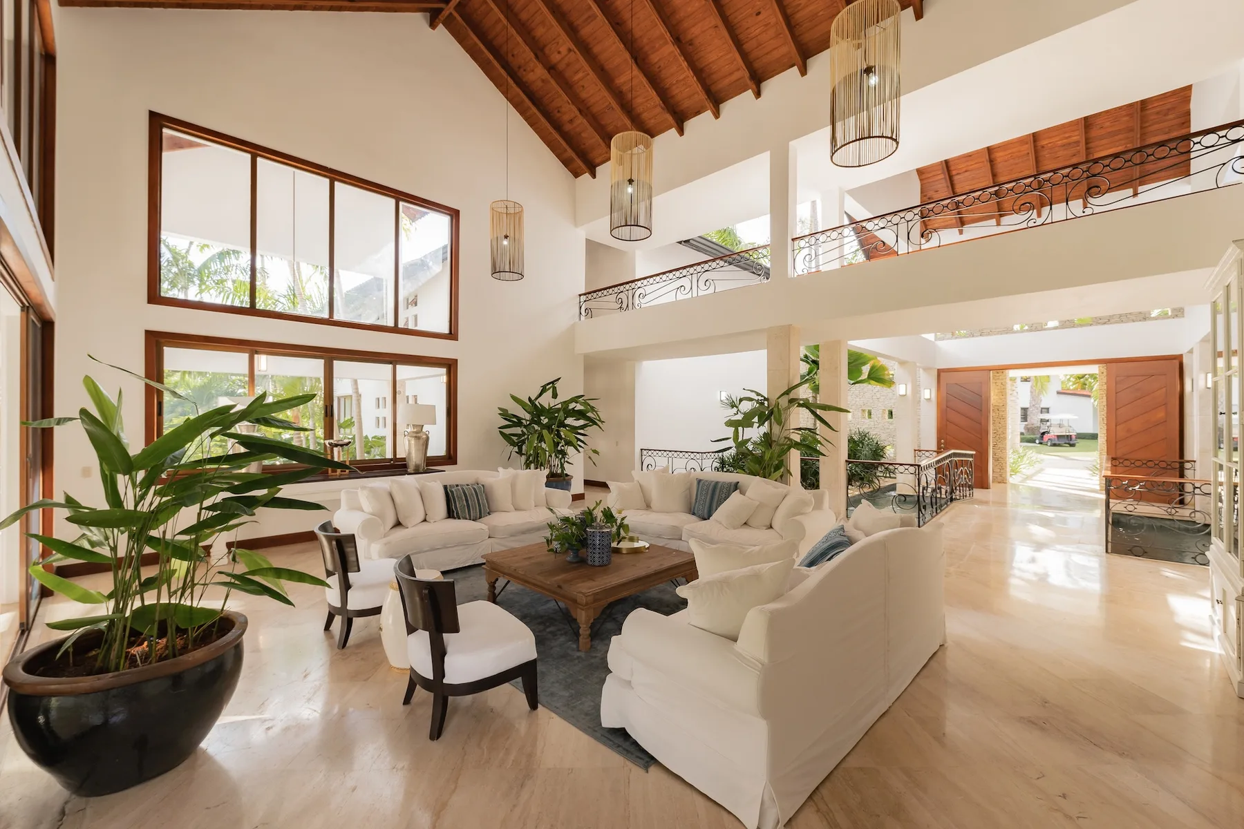 A spacious living room with pale seating, a wooden coffee table, and tall windows.