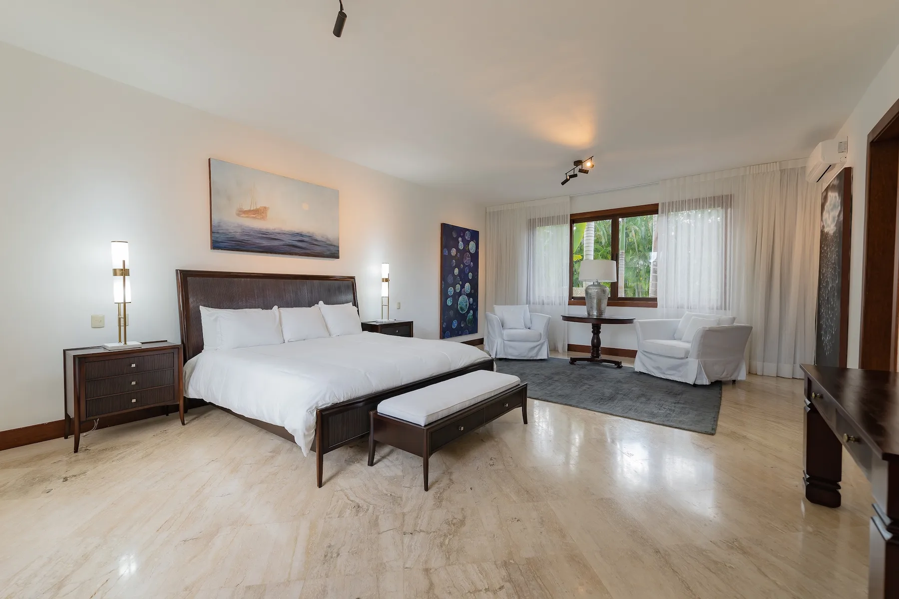 A bedroom with a large bed and a sitting area beside the window.