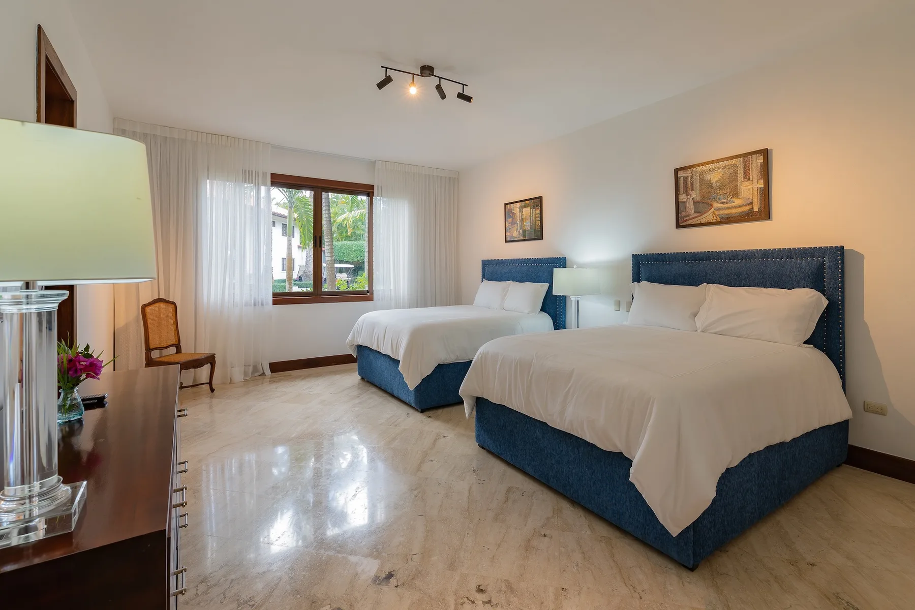 A bedroom with two beds, white bedding, and a window with sheer curtains.