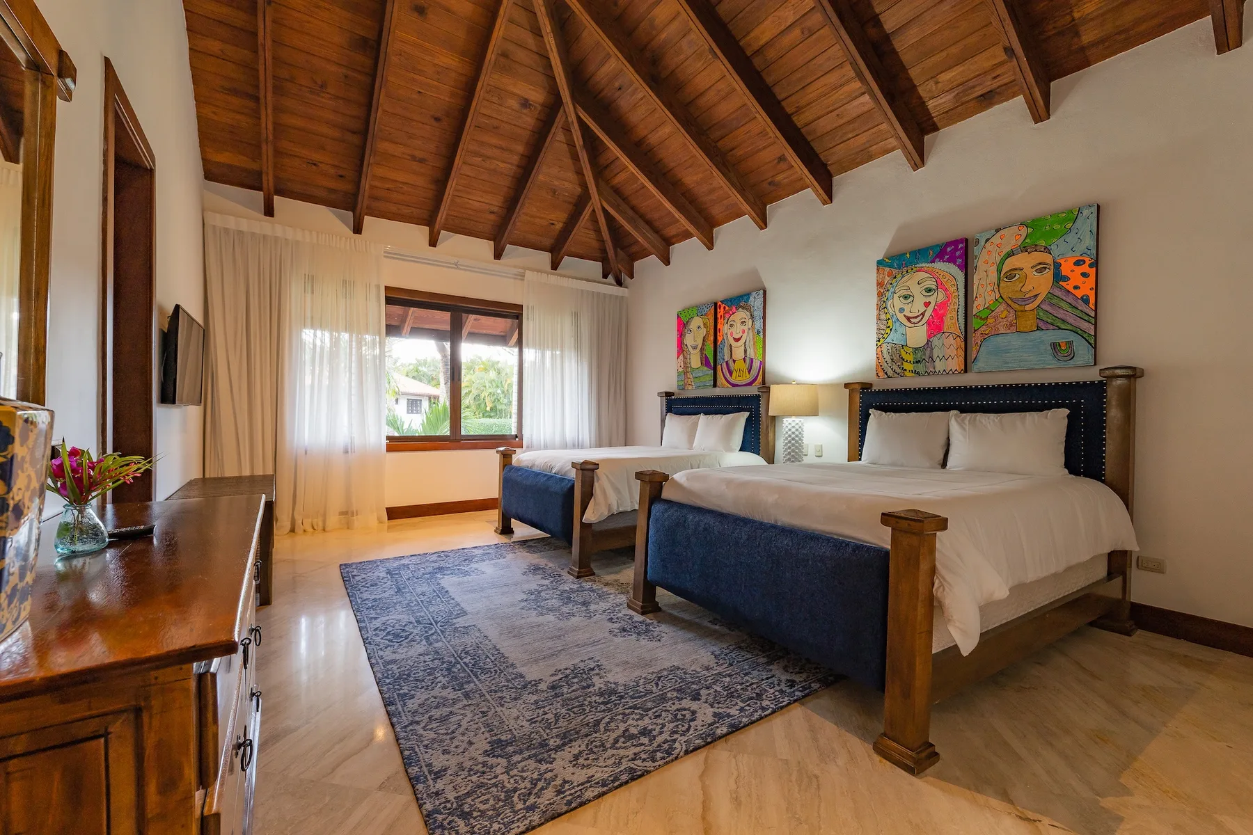 A bedroom with two beds, a patterned rug, and colorful artwork above the headboards.