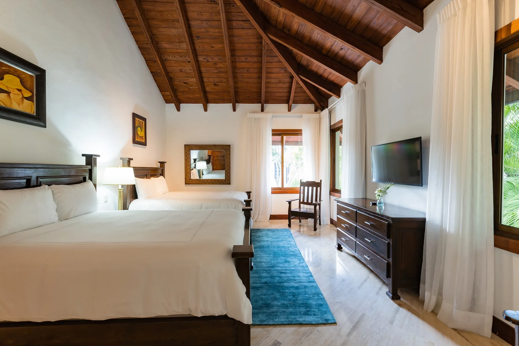A bedroom with a bed, a blue rug, and a television on a dresser.