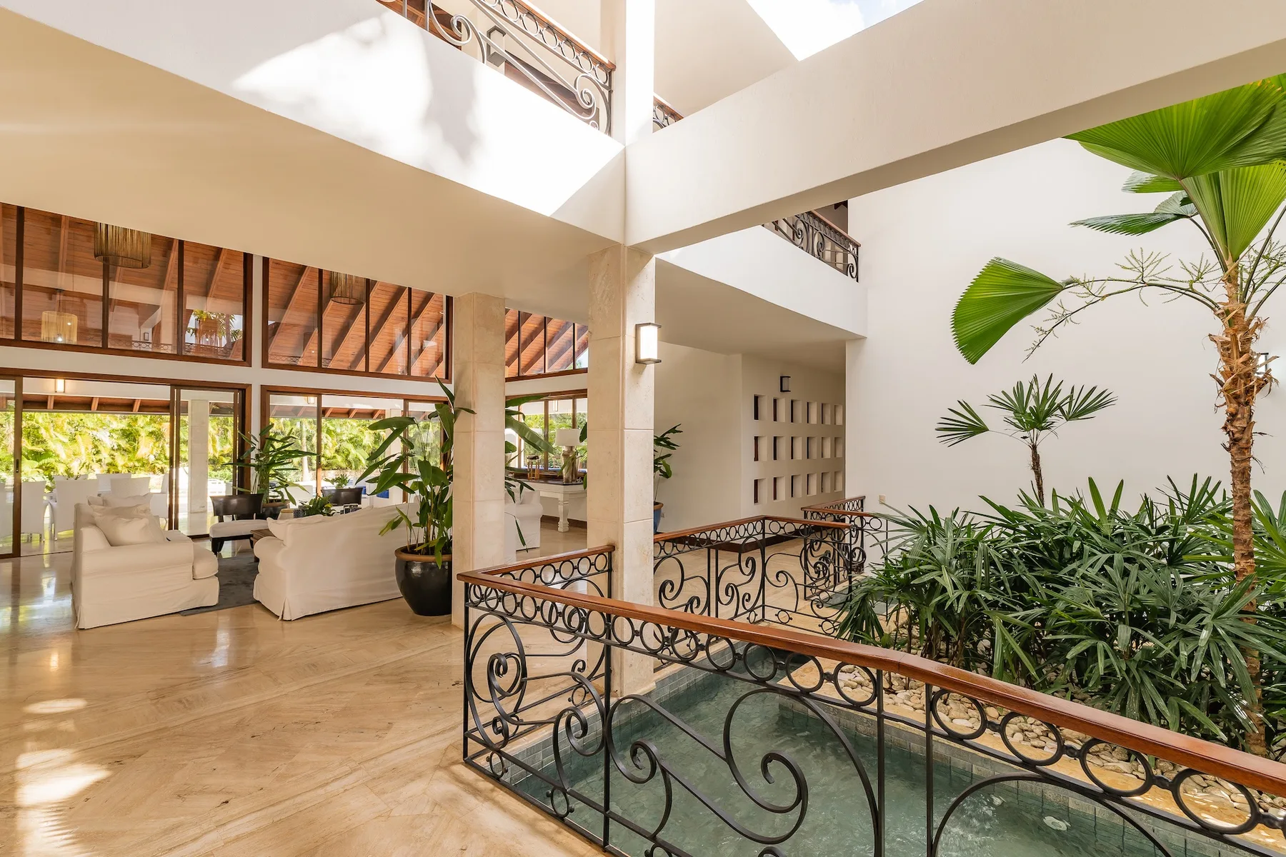 Un patio interior luminoso con barandillas decorativas, plantas tropicales y asientos.