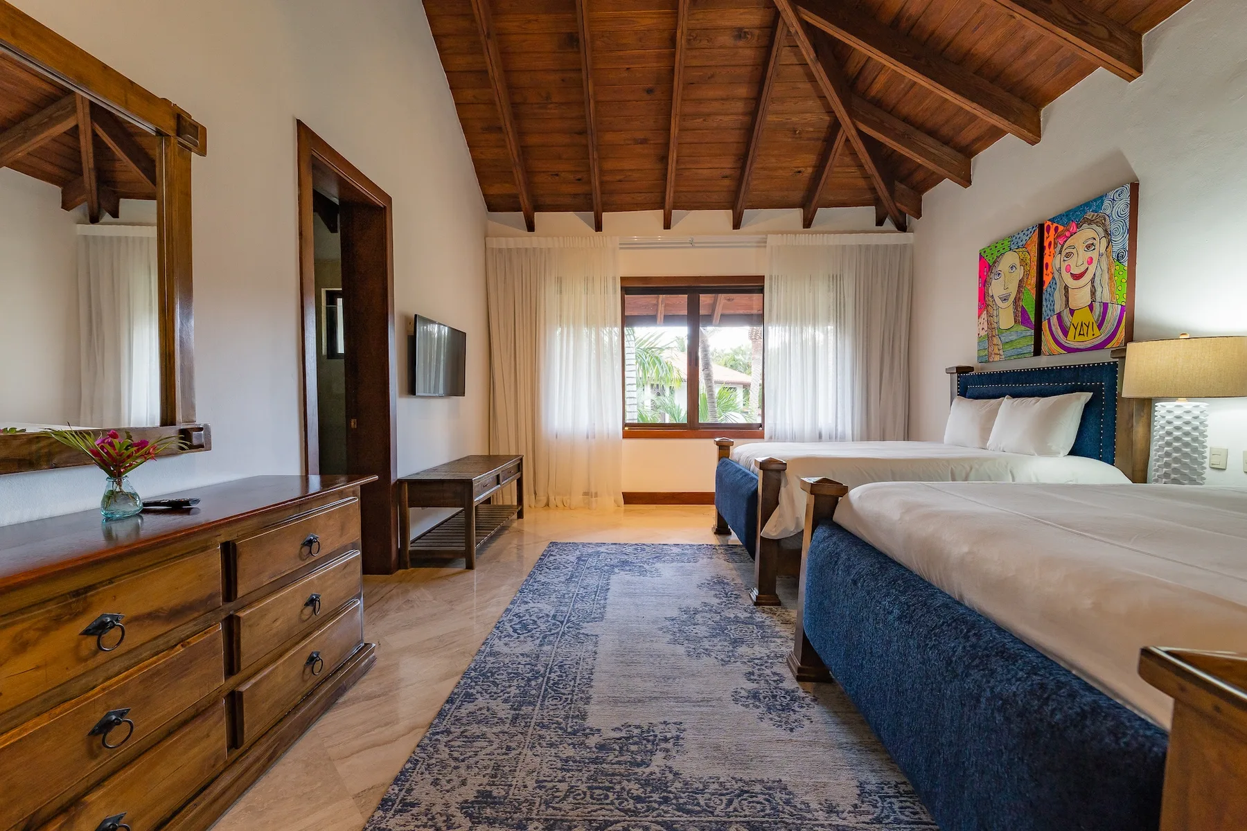 A bedroom with two beds, a window, and a patterned rug.