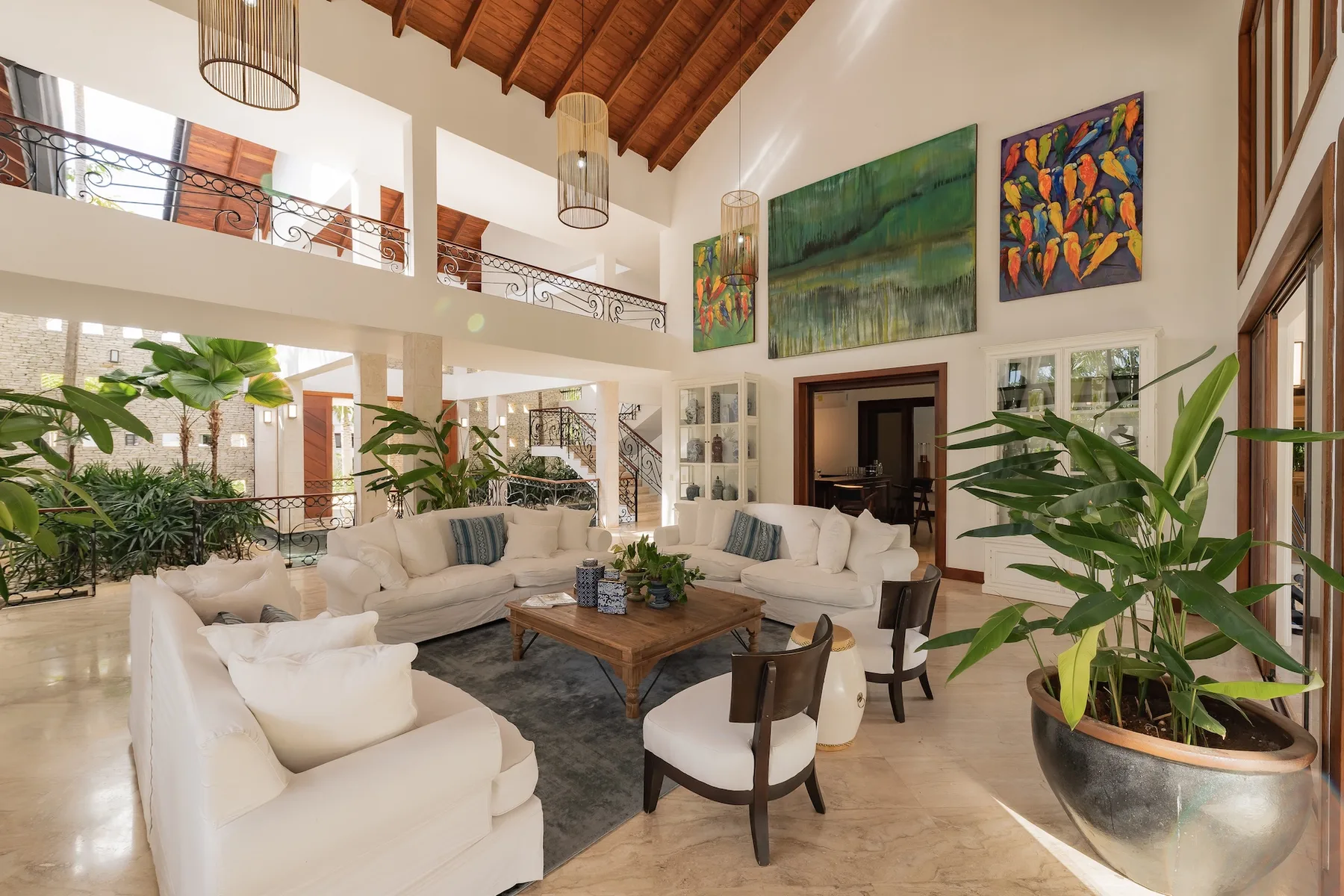 A bright, high-ceiling living room with seating and large plants.