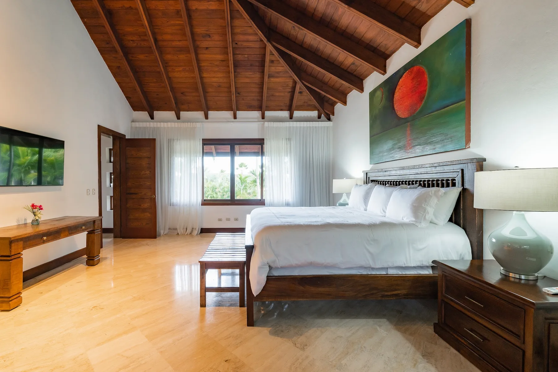 A bedroom with a large bed beneath a high wooden ceiling.