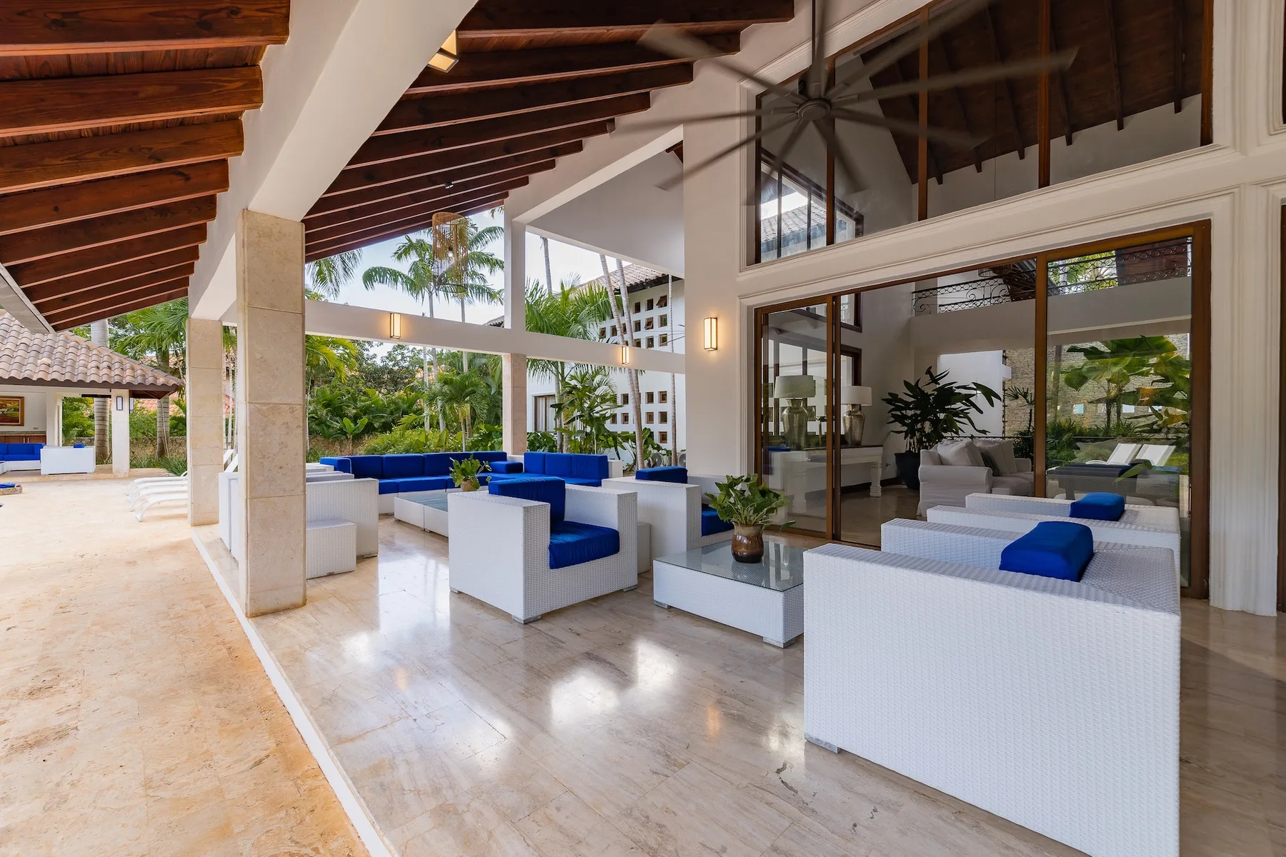 An open-air lounge with white seating and blue cushions beside a glass wall.