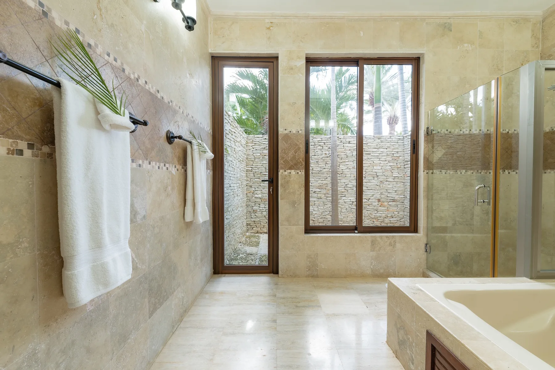 A tiled bathroom with a glass shower, bathtub, and windows overlooking greenery.
