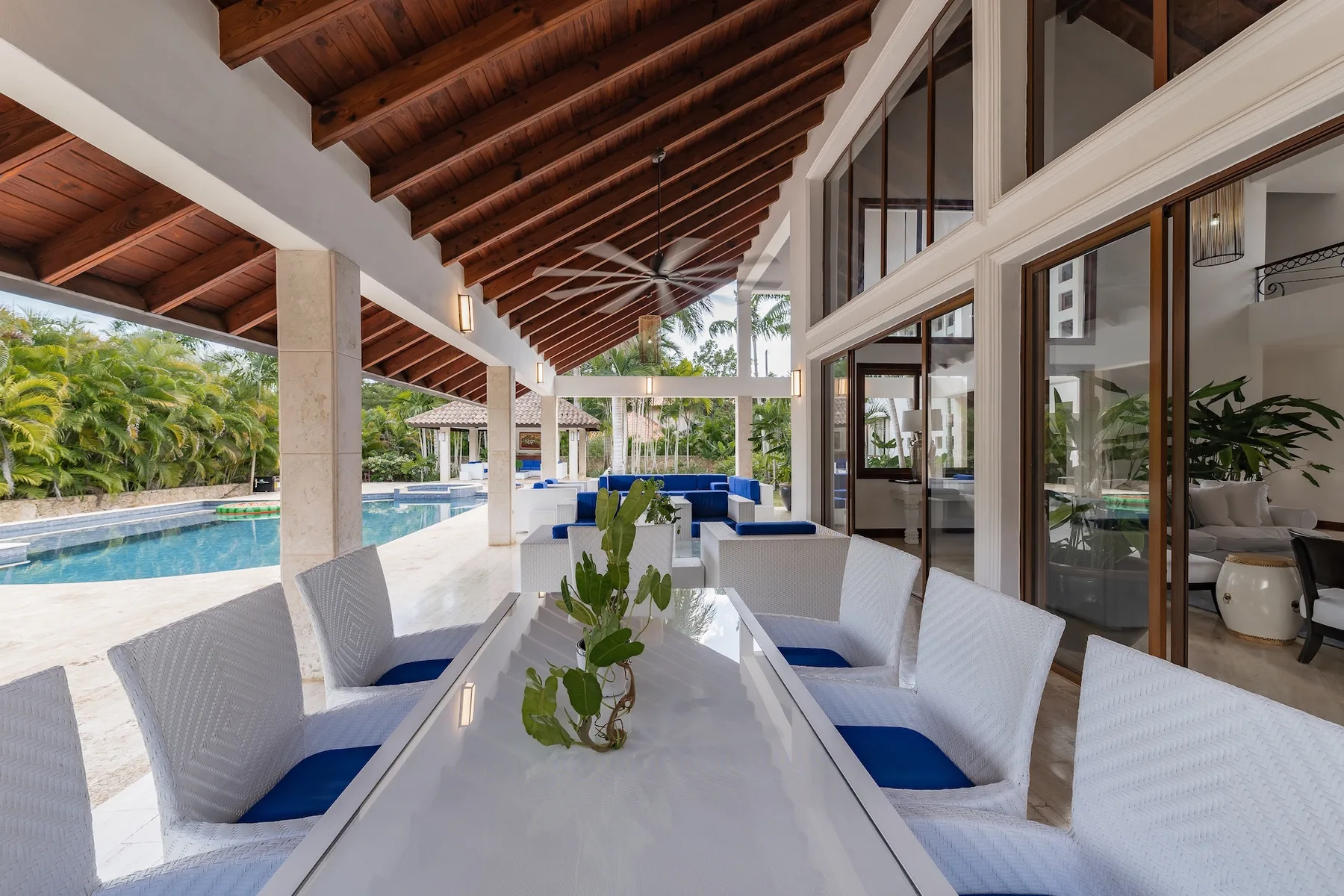 A covered outdoor dining area with a long table beside a swimming pool.