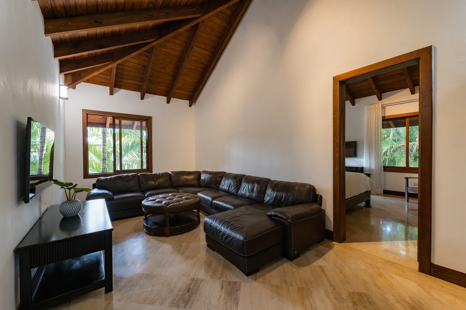 A living room with dark seating, a round coffee table, and large windows.