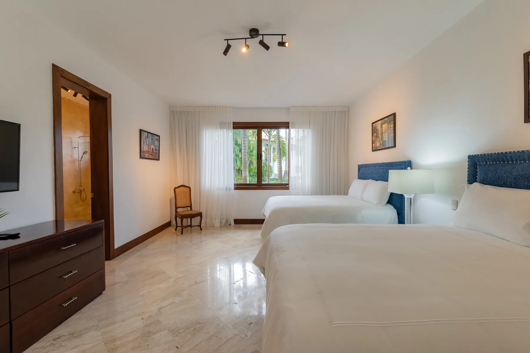 A bedroom with two beds, a window, and a chair.