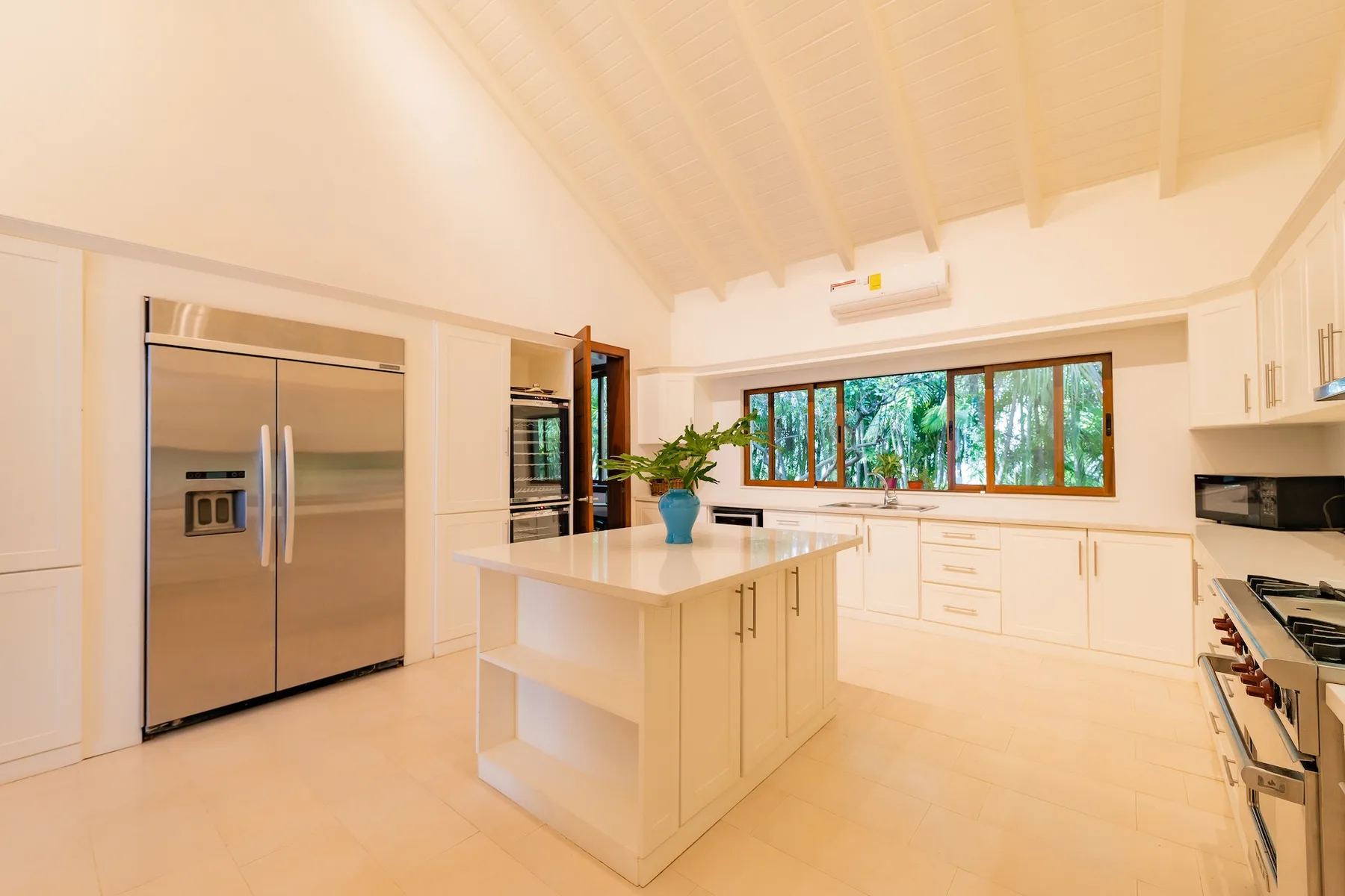 A bright kitchen with a central island, light cabinets, and wide windows.