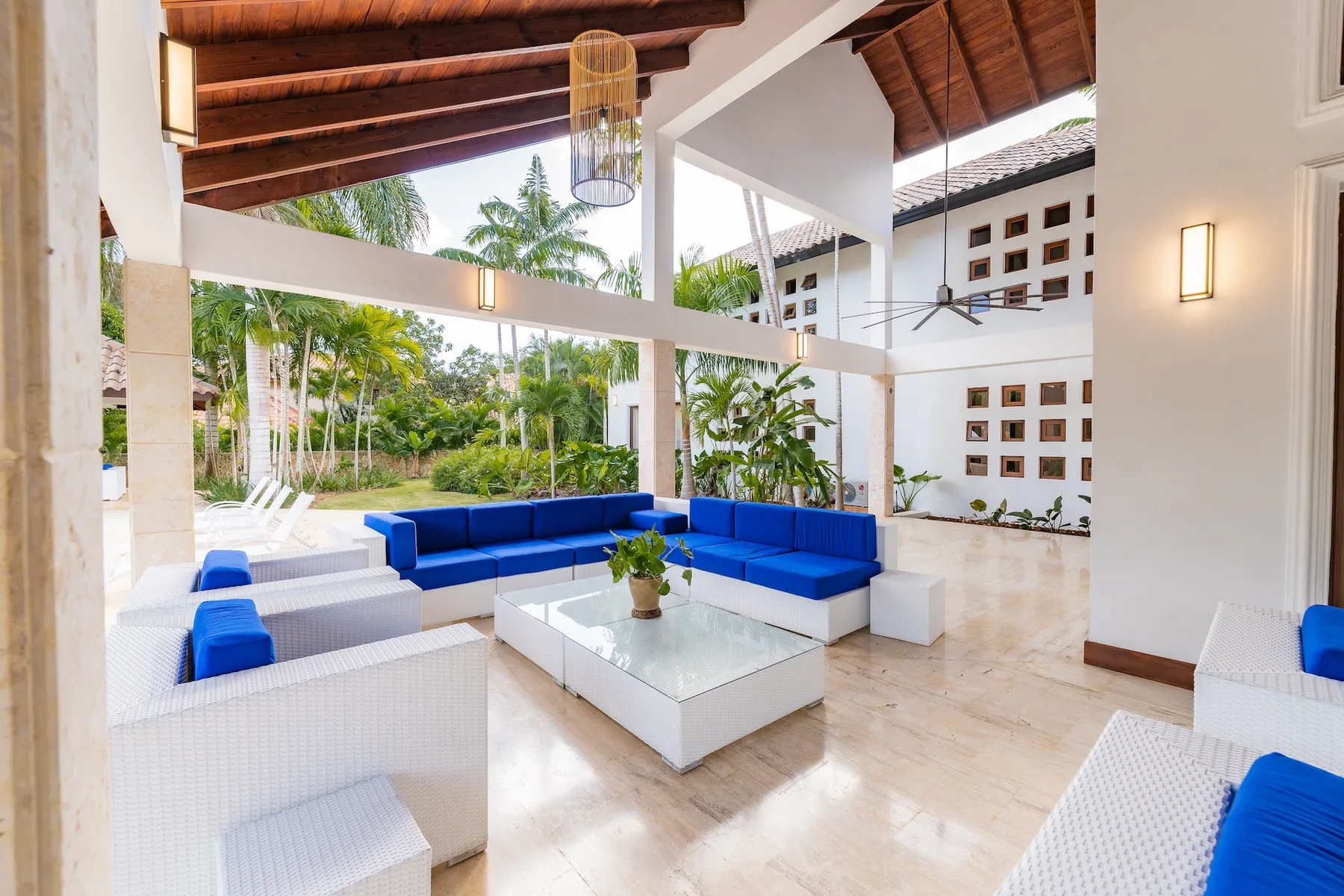An open lounge with blue seating and a glass coffee table faces a garden.