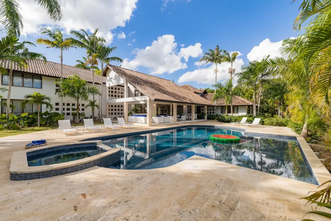A swimming pool and adjoining hot tub sit beside a palm-lined resort building.