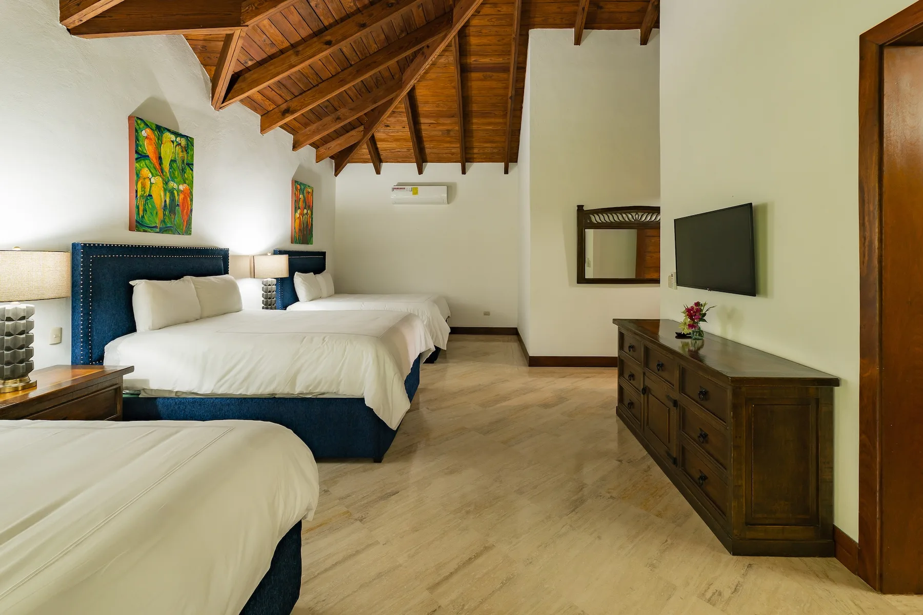 A bedroom with white bedding beneath an exposed wooden ceiling.