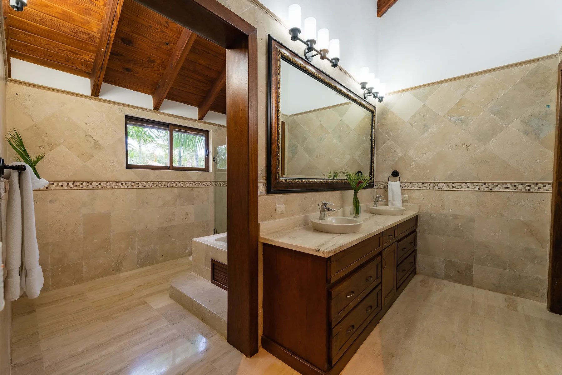 A bathroom with a wood vanity, large mirror, and tiled walls.
