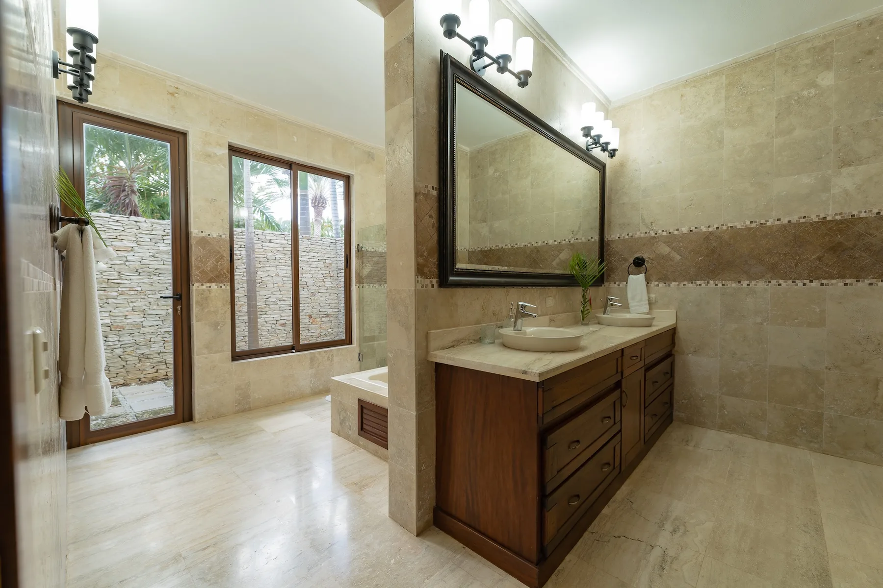 A bright bathroom with a wood vanity, large mirror, and glass doors.
