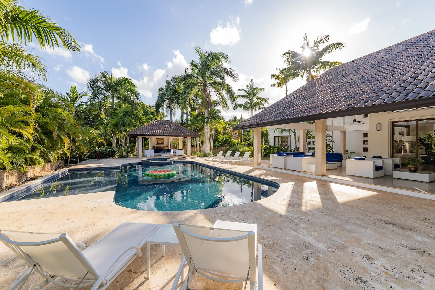 A tropical pool courtyard with lounge seating and a covered outdoor dining area.